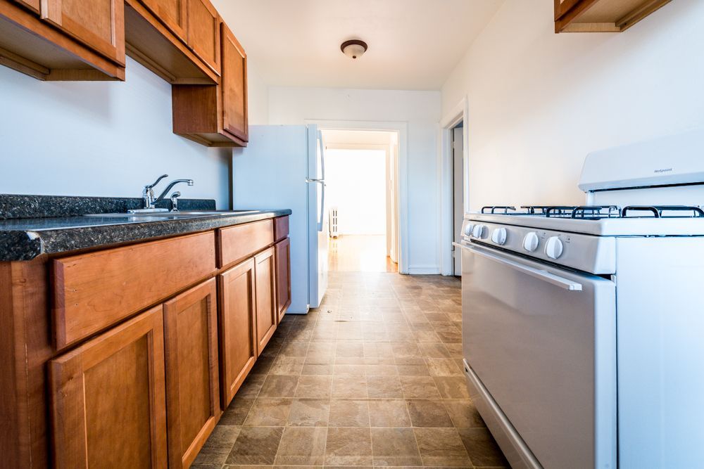 Kitchen with wooden cabinets, white appliances, and a view into a hallway.