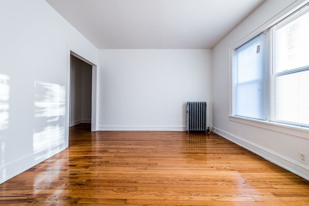 Empty room with hardwood floors, white walls, and a radiator by the window.