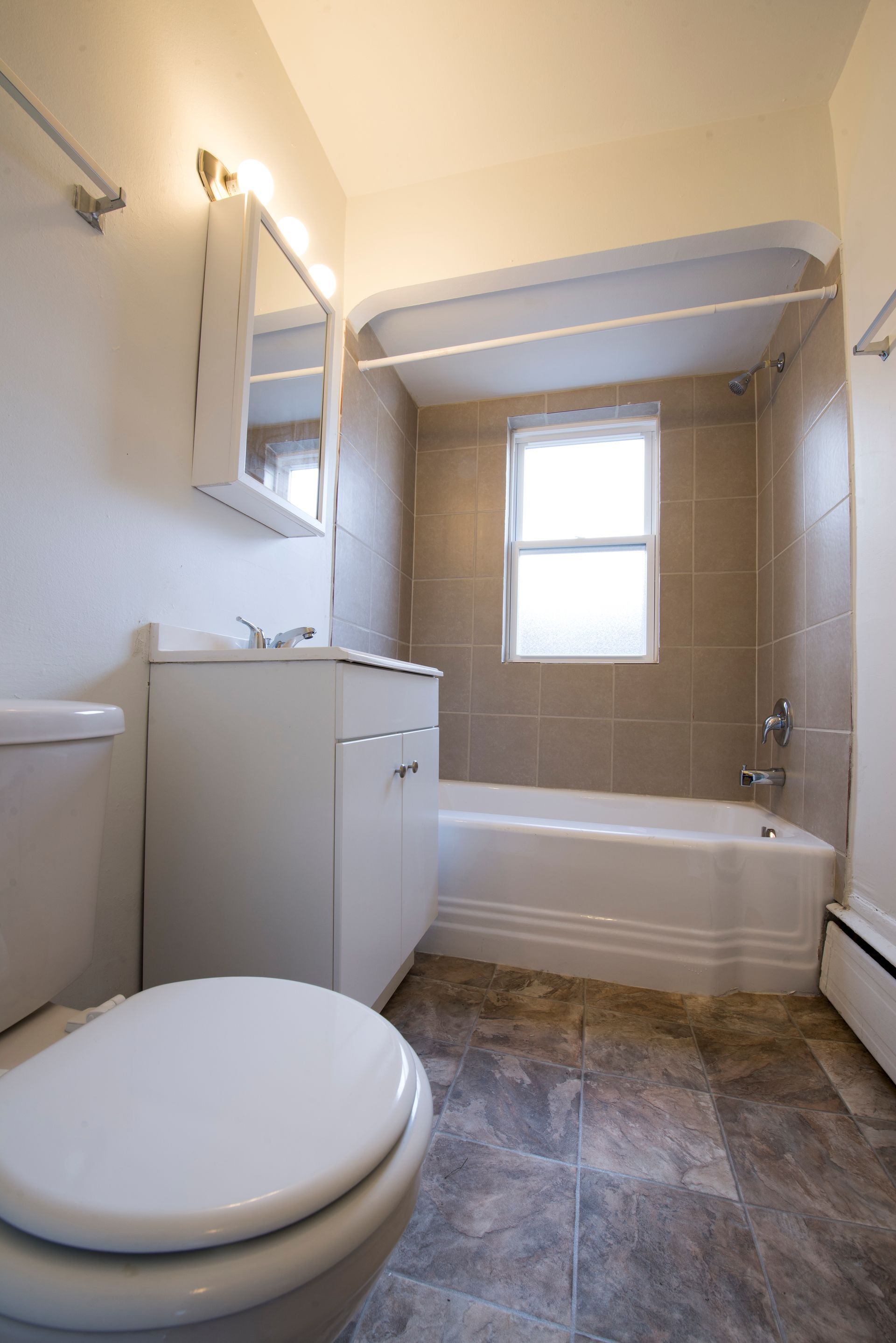 Bathroom with white toilet, vanity, bathtub, and neutral tile walls.