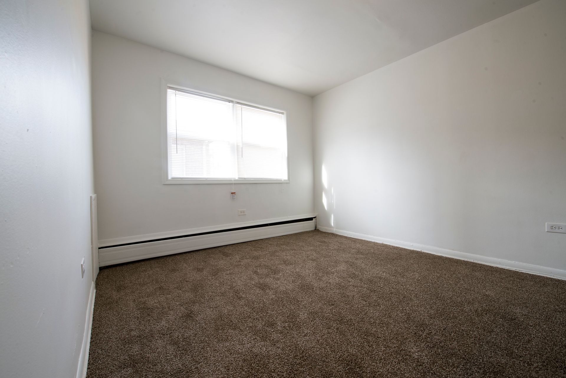 Empty room with brown carpet, white walls, and a window with blinds.