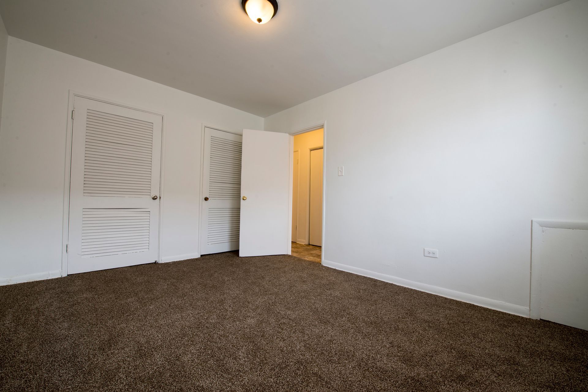 Empty bedroom with brown carpet, white walls, and two doors.
