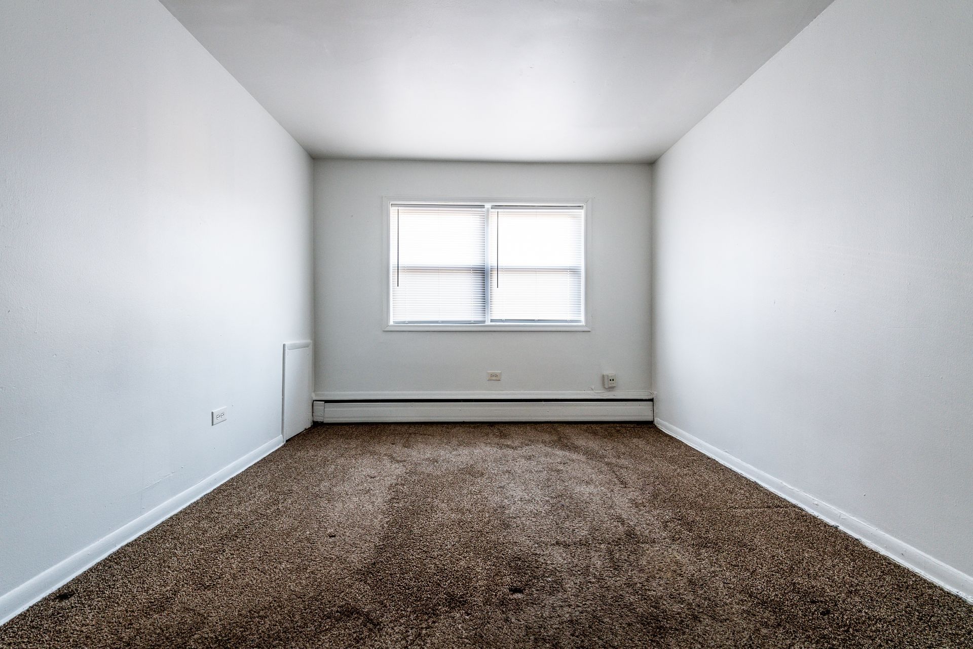 Empty room with brown carpet, white walls, and a window.