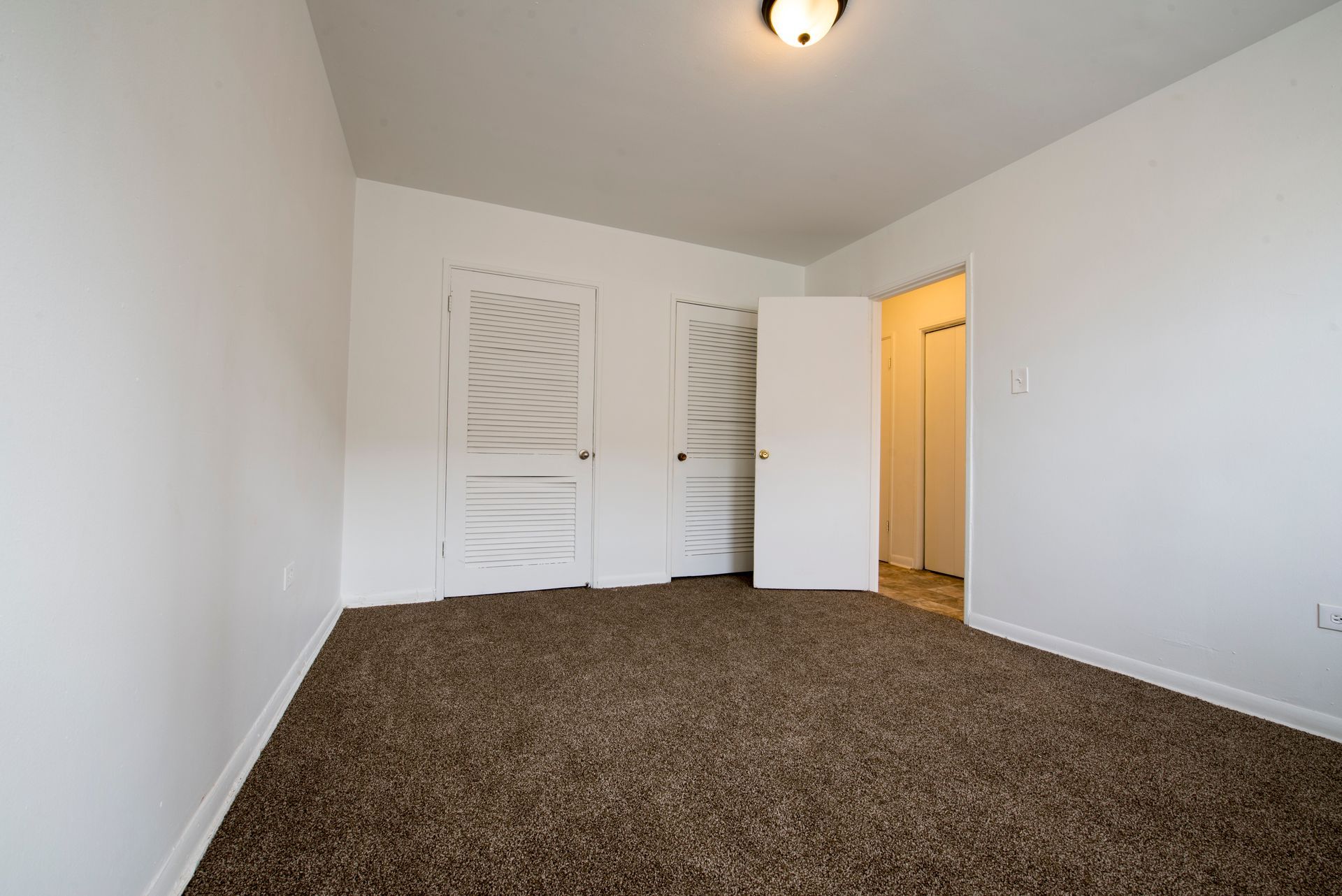 Empty room with brown carpet, white walls, two closet doors, and a doorway.