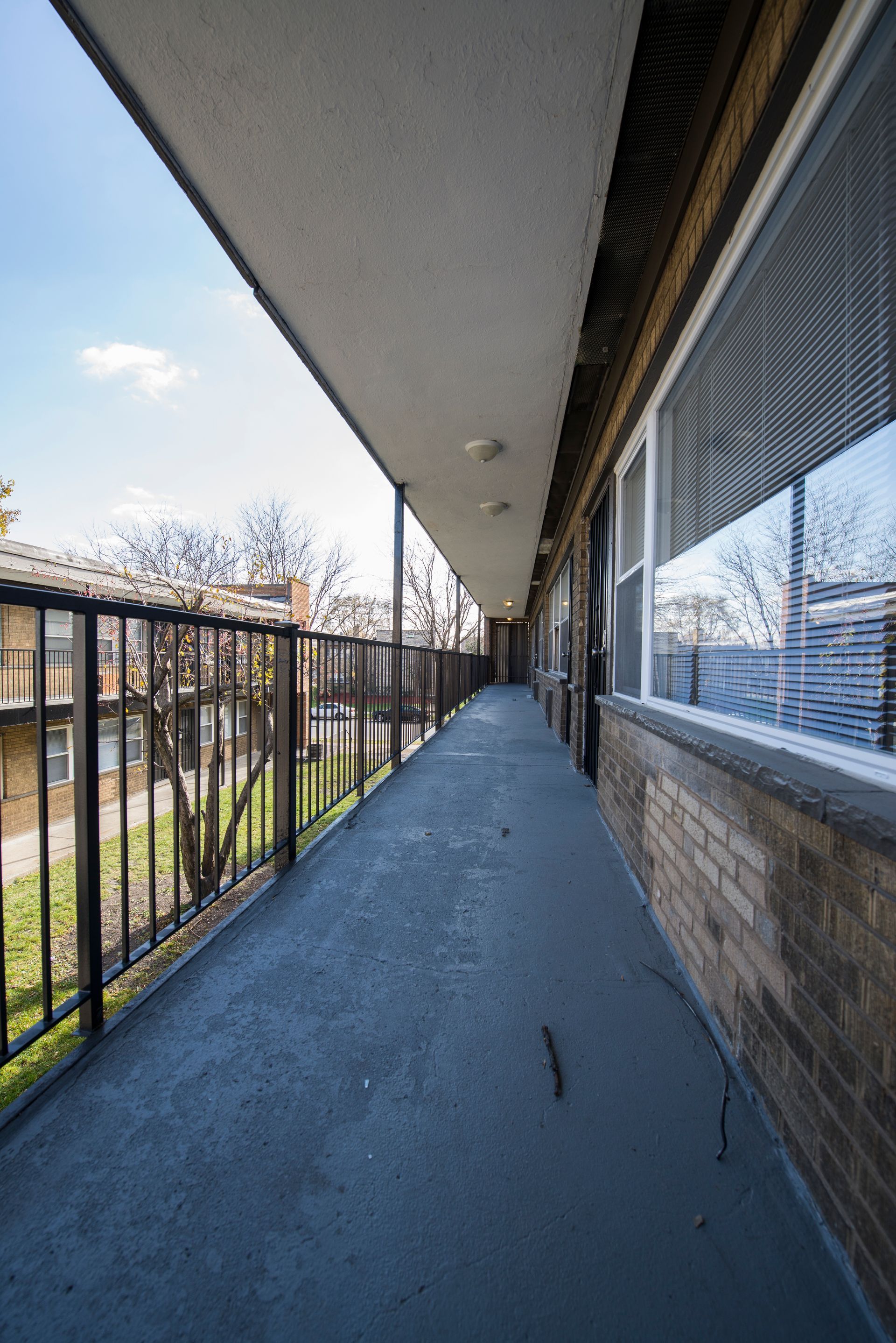 Exterior apartment hallway with railing, windows, and long view.