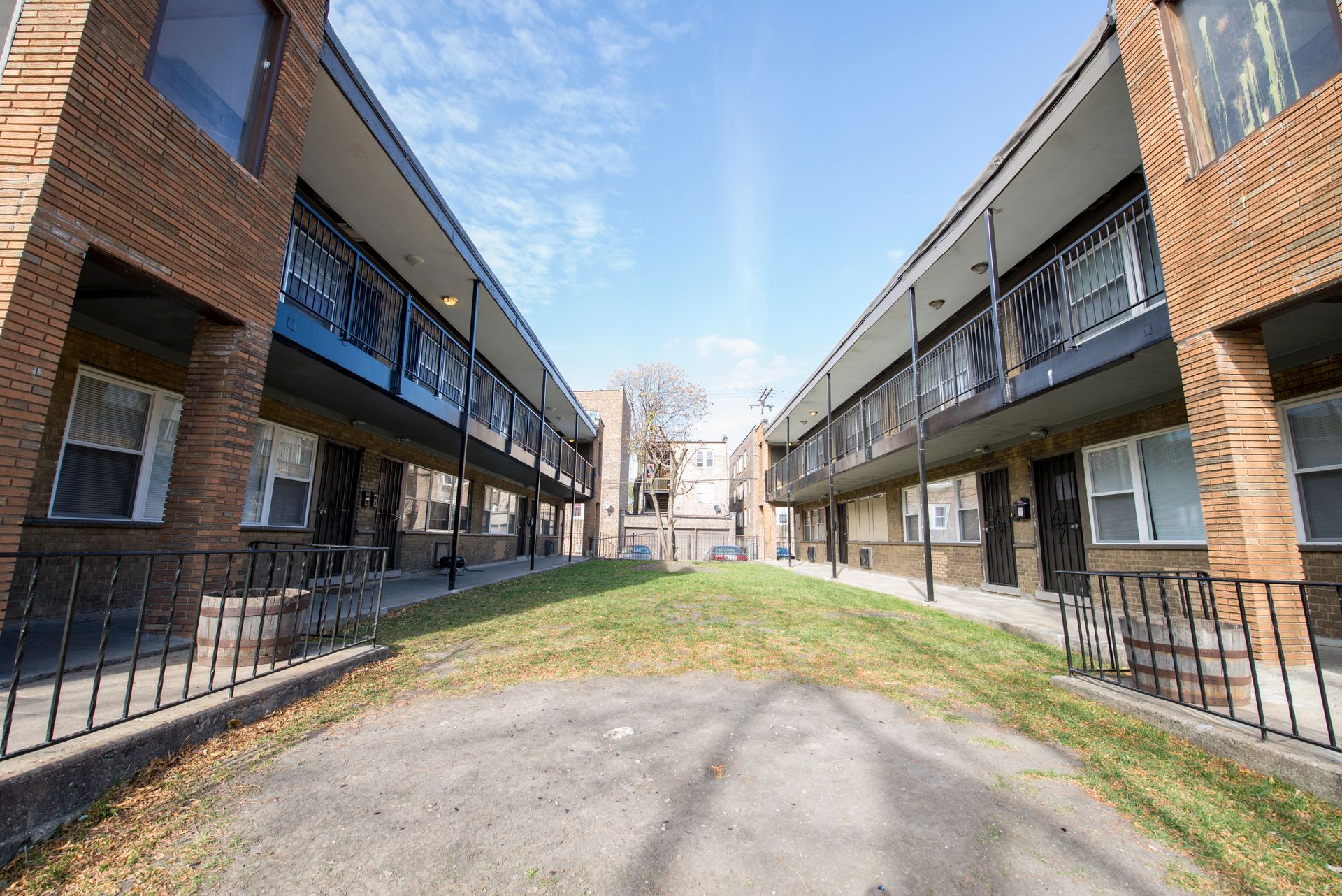 Two-story brick apartment buildings facing each other, with a grassy area and walkway in between.