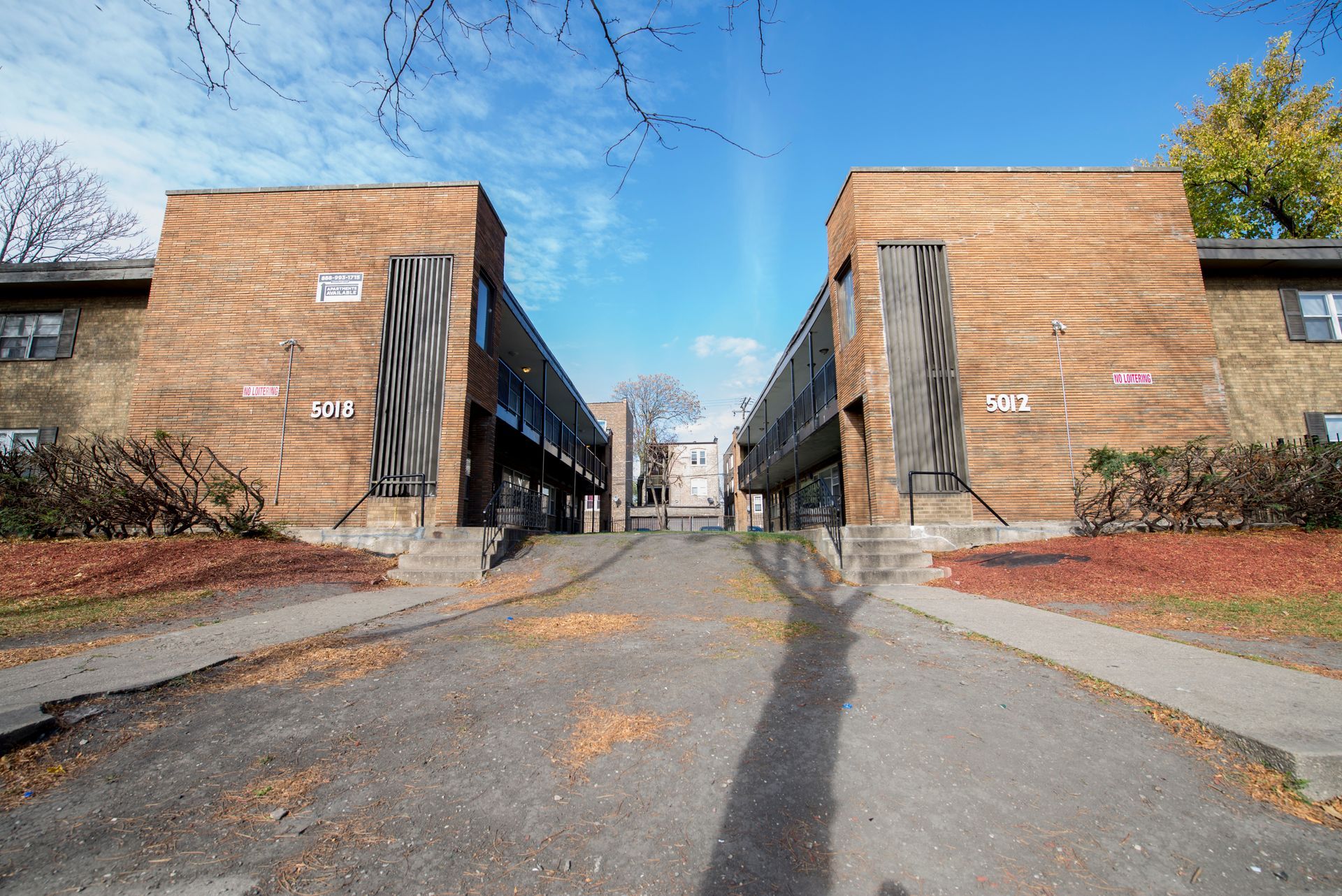 Two brown brick apartment buildings facing each other, driveway between them, sunny day.