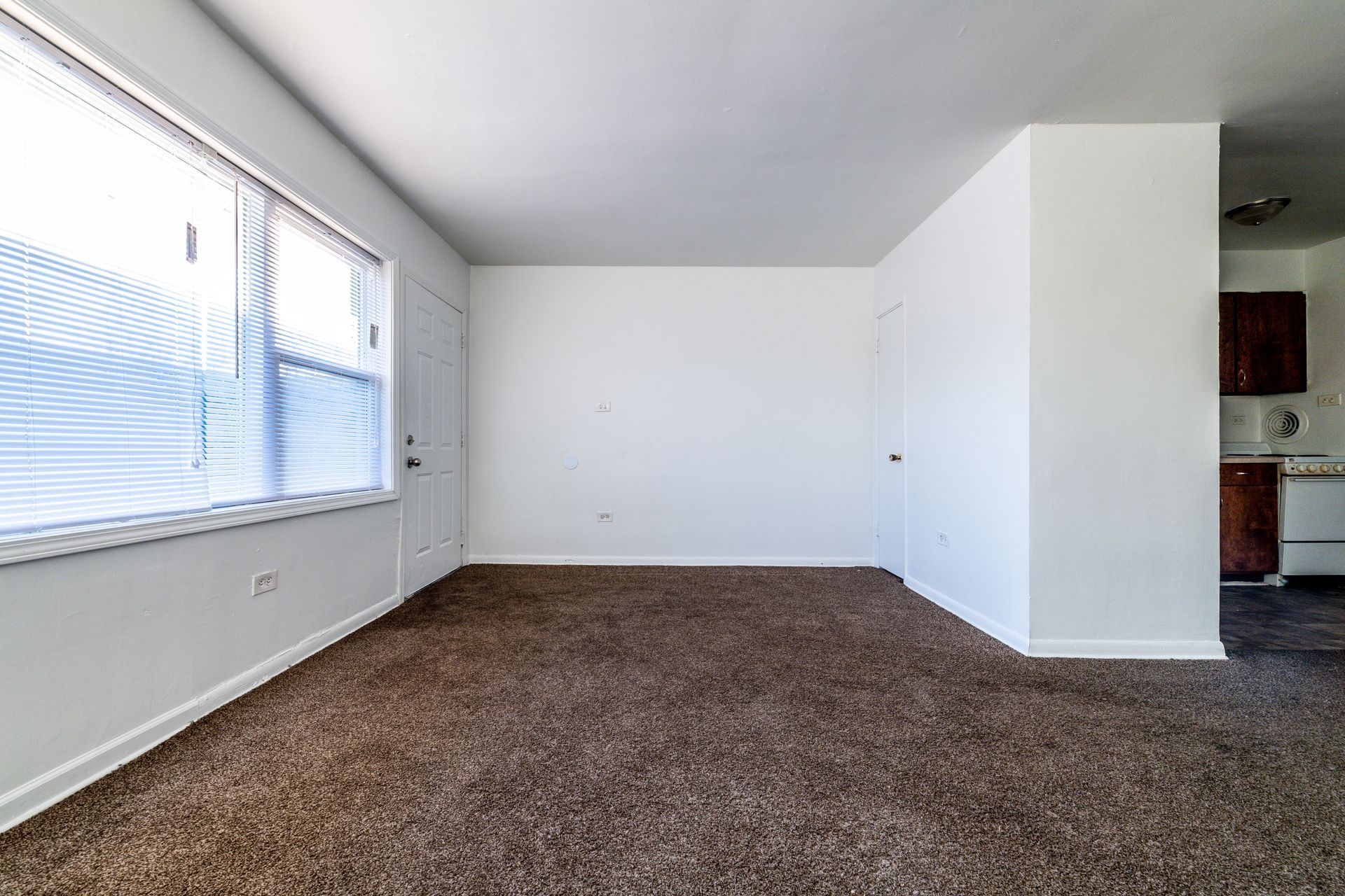 Empty room with brown carpet, large window, and white walls.