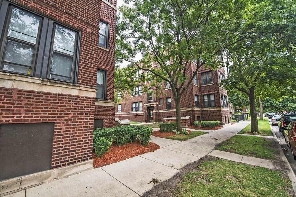 Red brick apartment buildings with trees and a sidewalk.