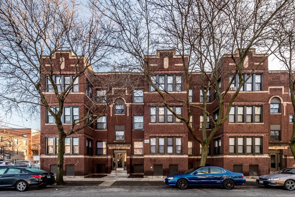Brick apartment building with parked cars on the street. Bare trees frame the facade.