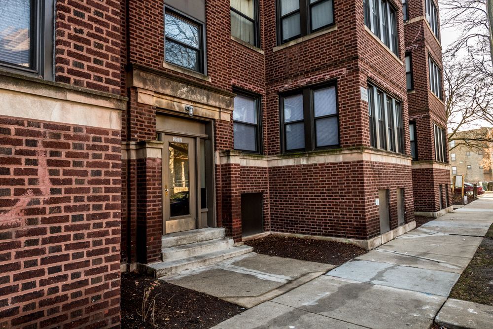 Brick apartment building with steps leading to the front door, next to a sidewalk.