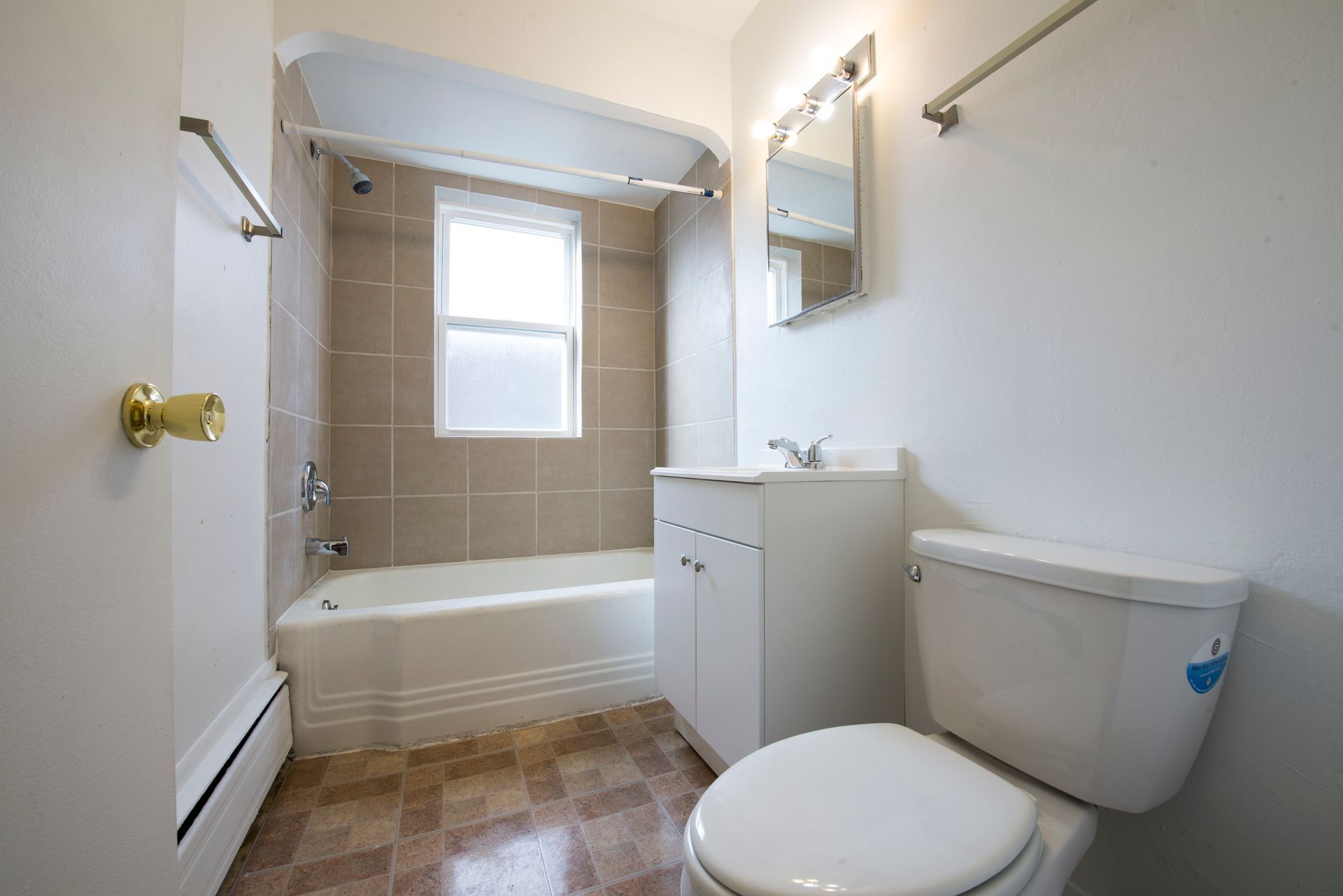 Bathroom with white fixtures, beige tiled shower, and a small window.
