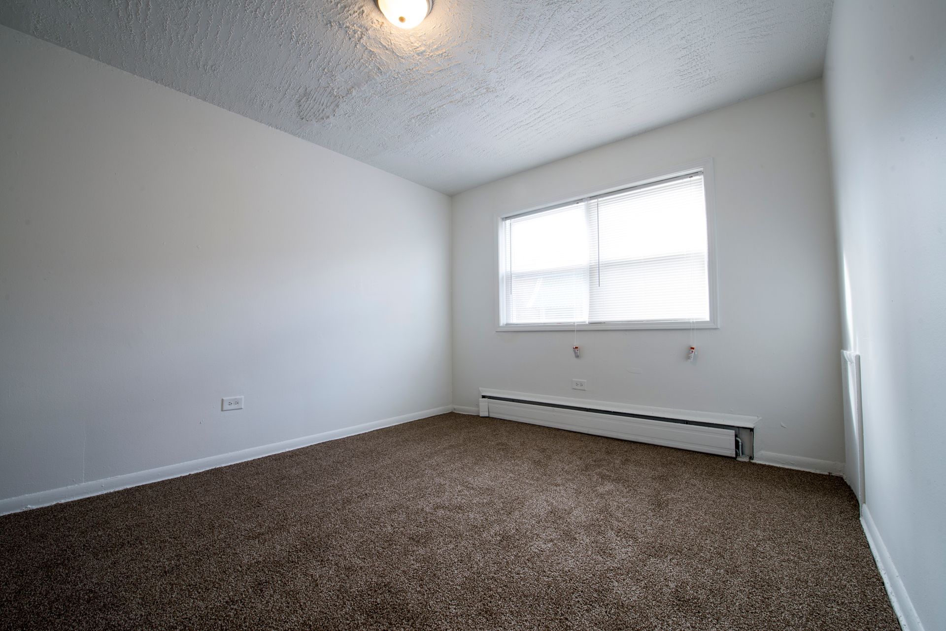 Empty room with brown carpet, white walls, and a window with blinds.