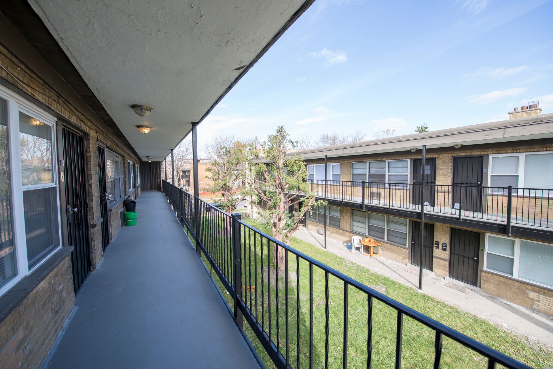Apartment building hallway with black railings, brick walls, and view of a grassy courtyard.