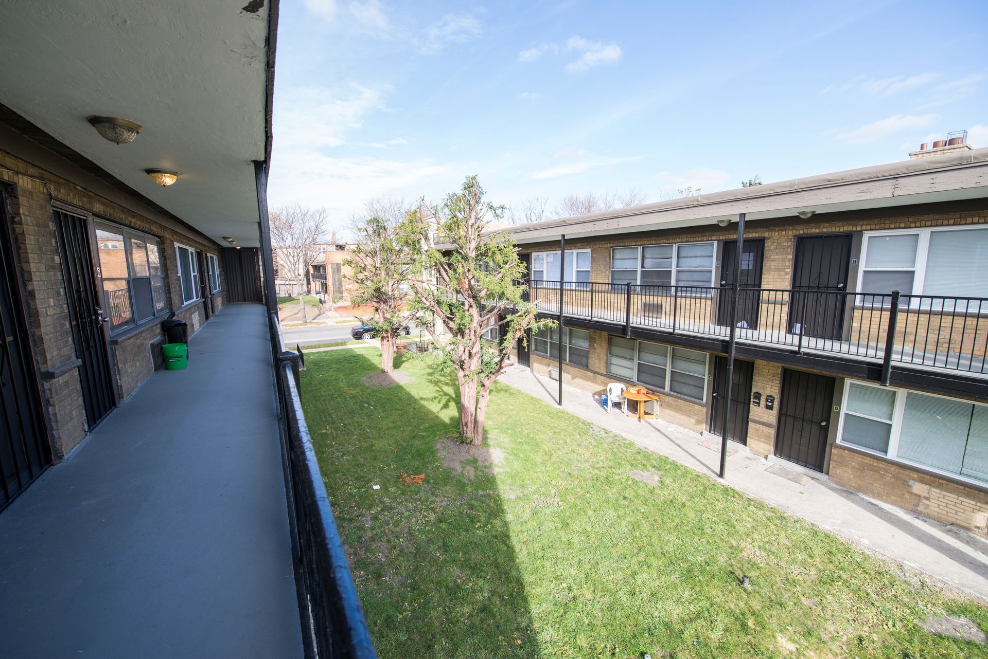Apartment buildings with central grassy courtyard, tree, and sunny sky.