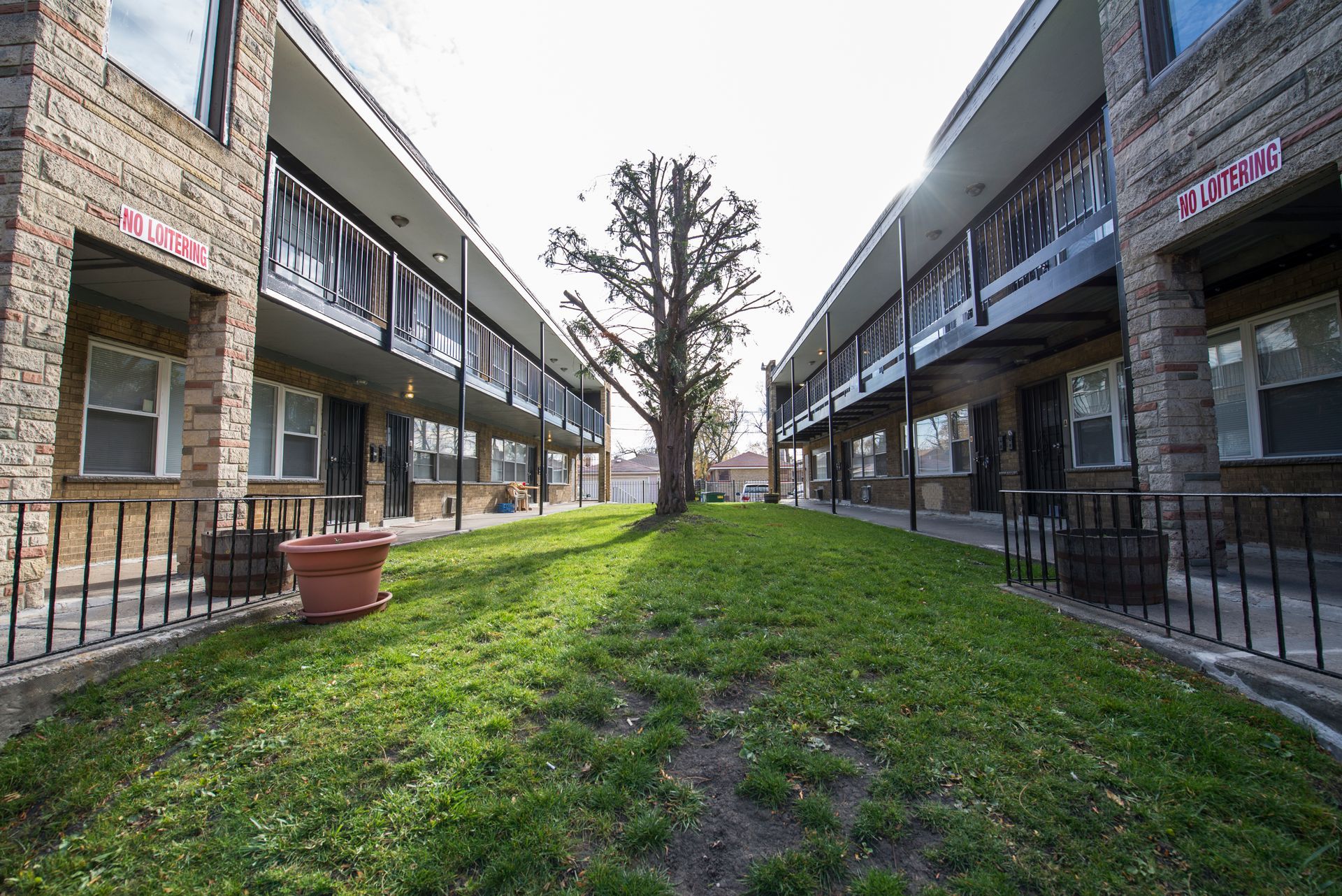 Two-story brick apartment buildings face each other, with a grassy area and tree between them.