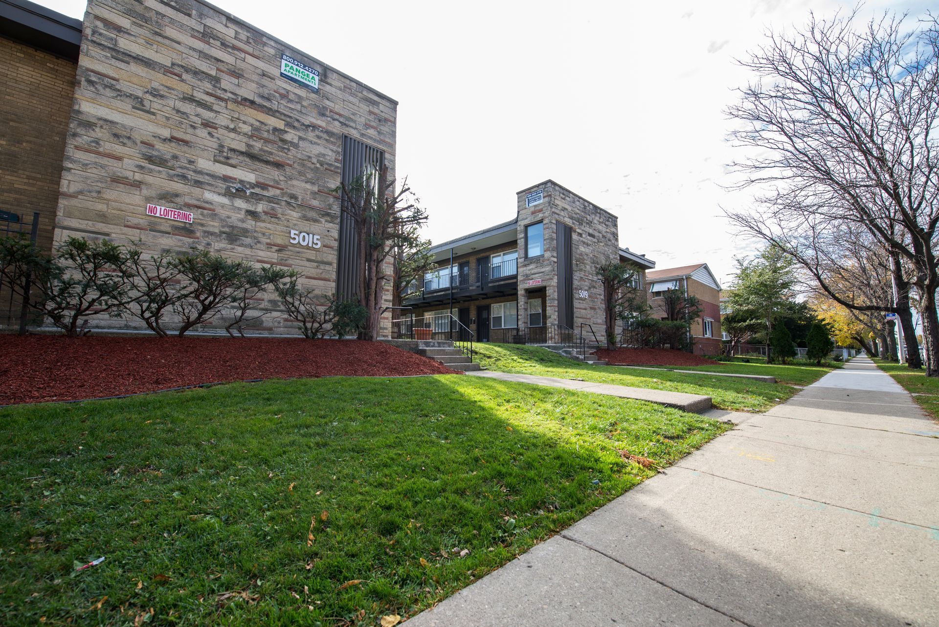 Apartment buildings with brick exteriors and a sidewalk on a grassy lawn.