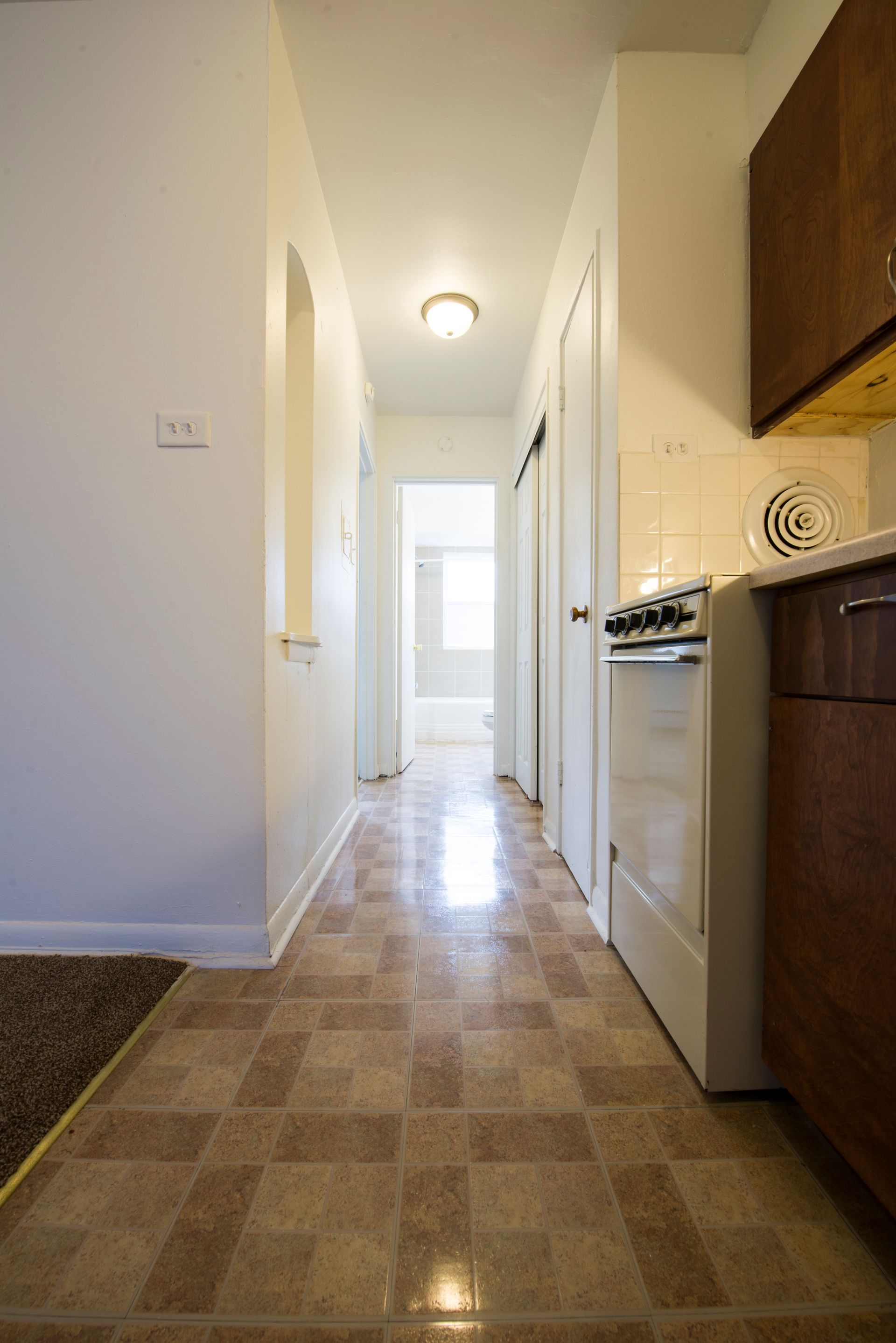 Hallway with brown tiled floor, white walls, and a stove to the right.