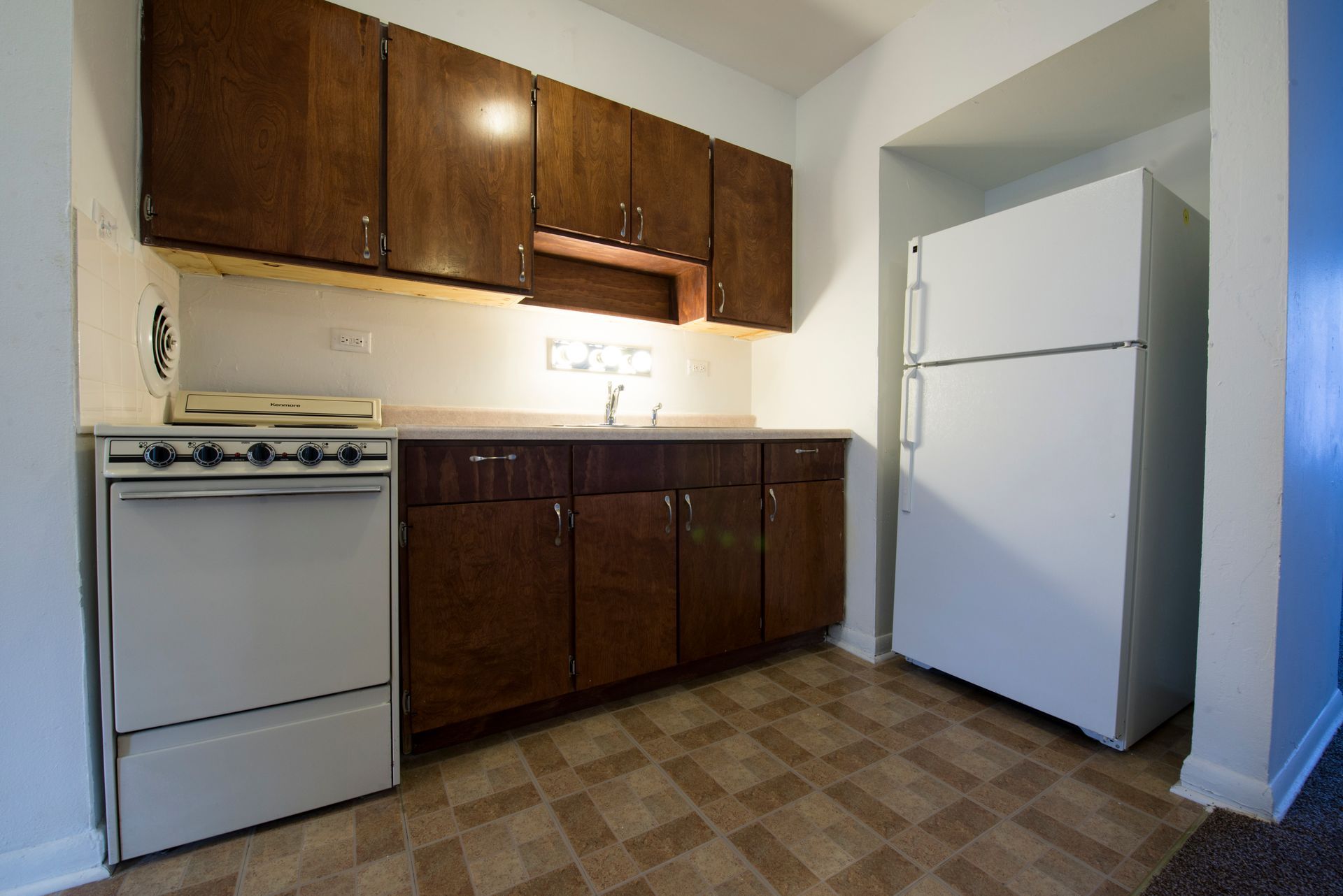 A small kitchen with brown cabinets, white appliances, and a tiled floor.