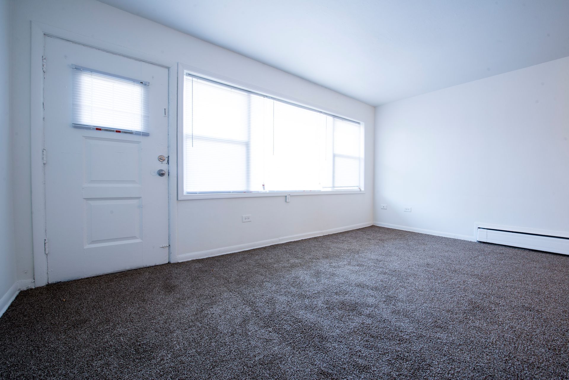 Empty room with beige carpet, white walls, a door, and a large window.