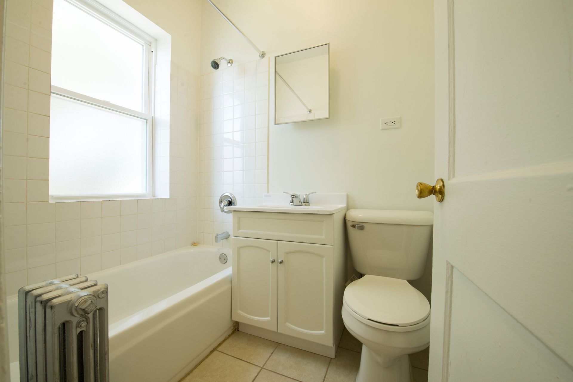 White bathroom with a bathtub, sink, toilet, window, and radiator.
