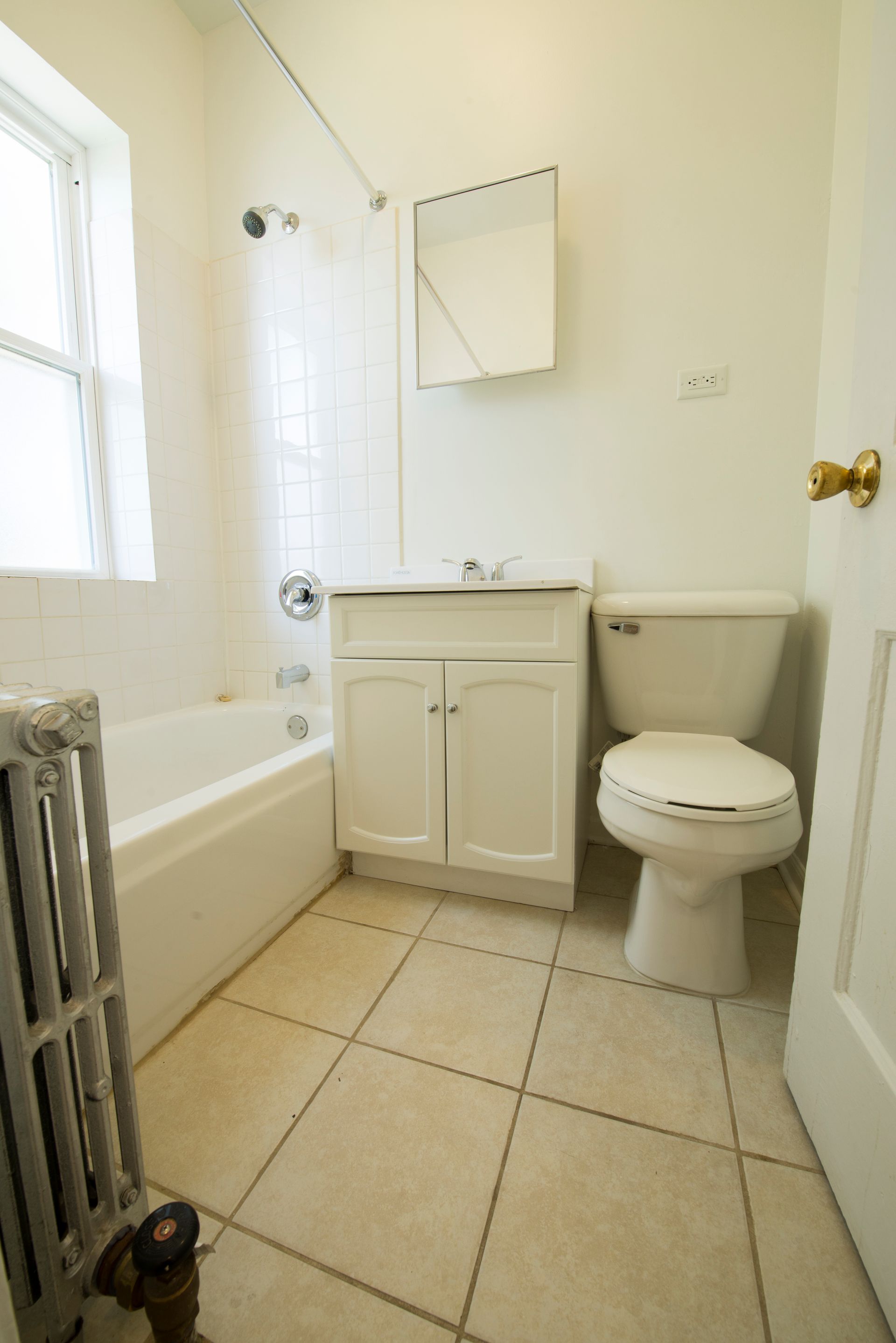 White bathroom with a tub, toilet, vanity, and a window.