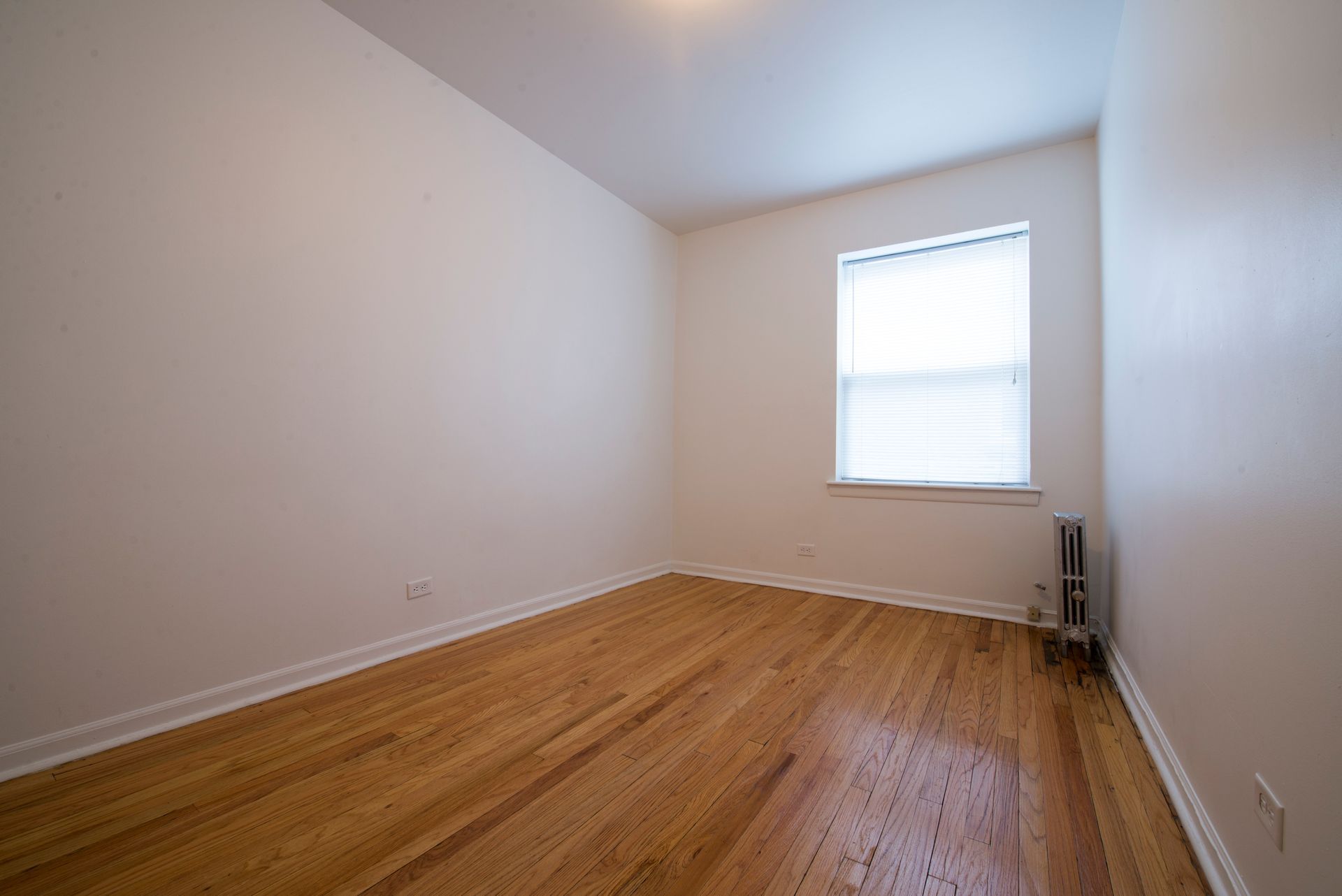 Empty room with hardwood floors, white walls, and a window with blinds.