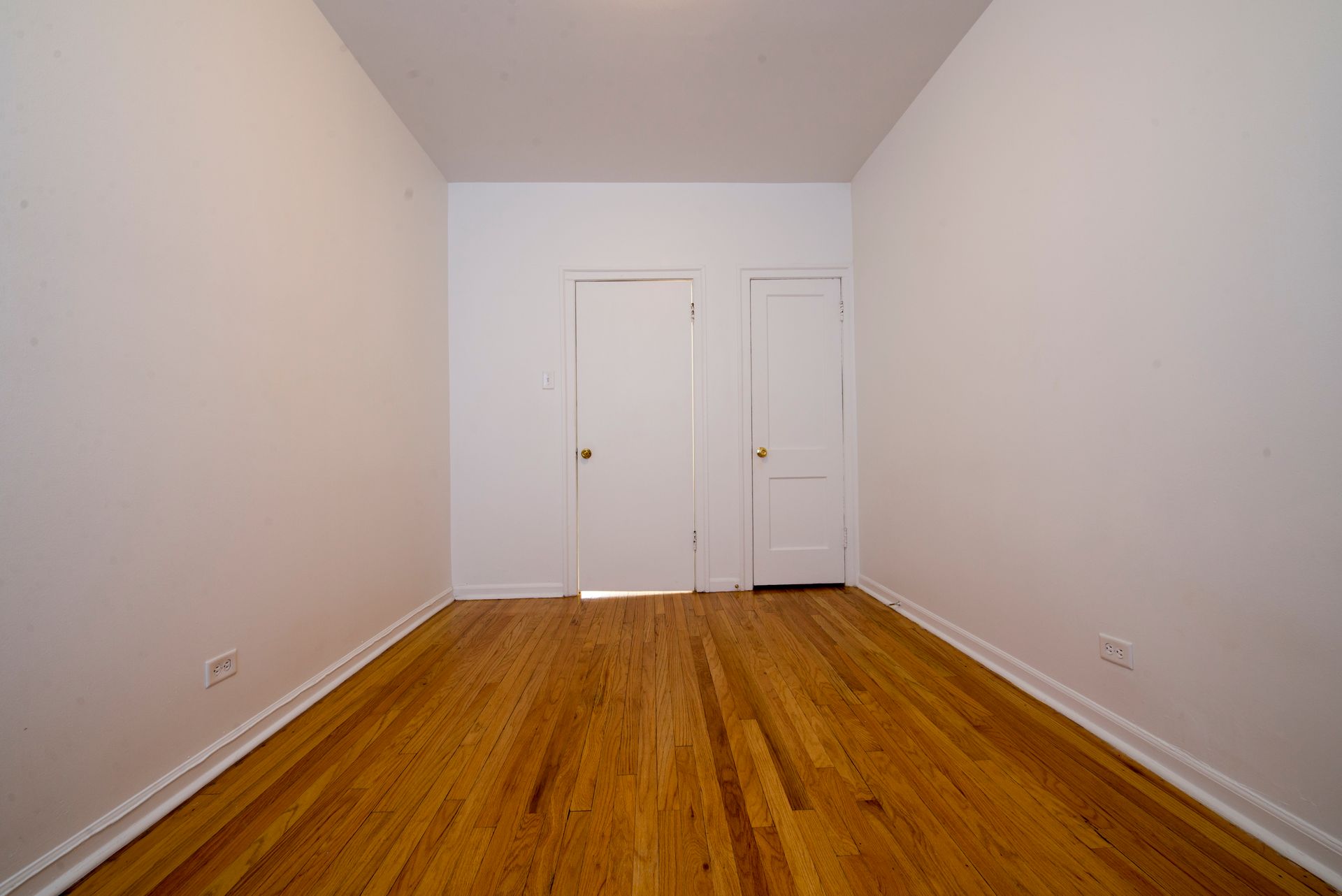 Empty room with hardwood floors, white walls, and two closed doors.