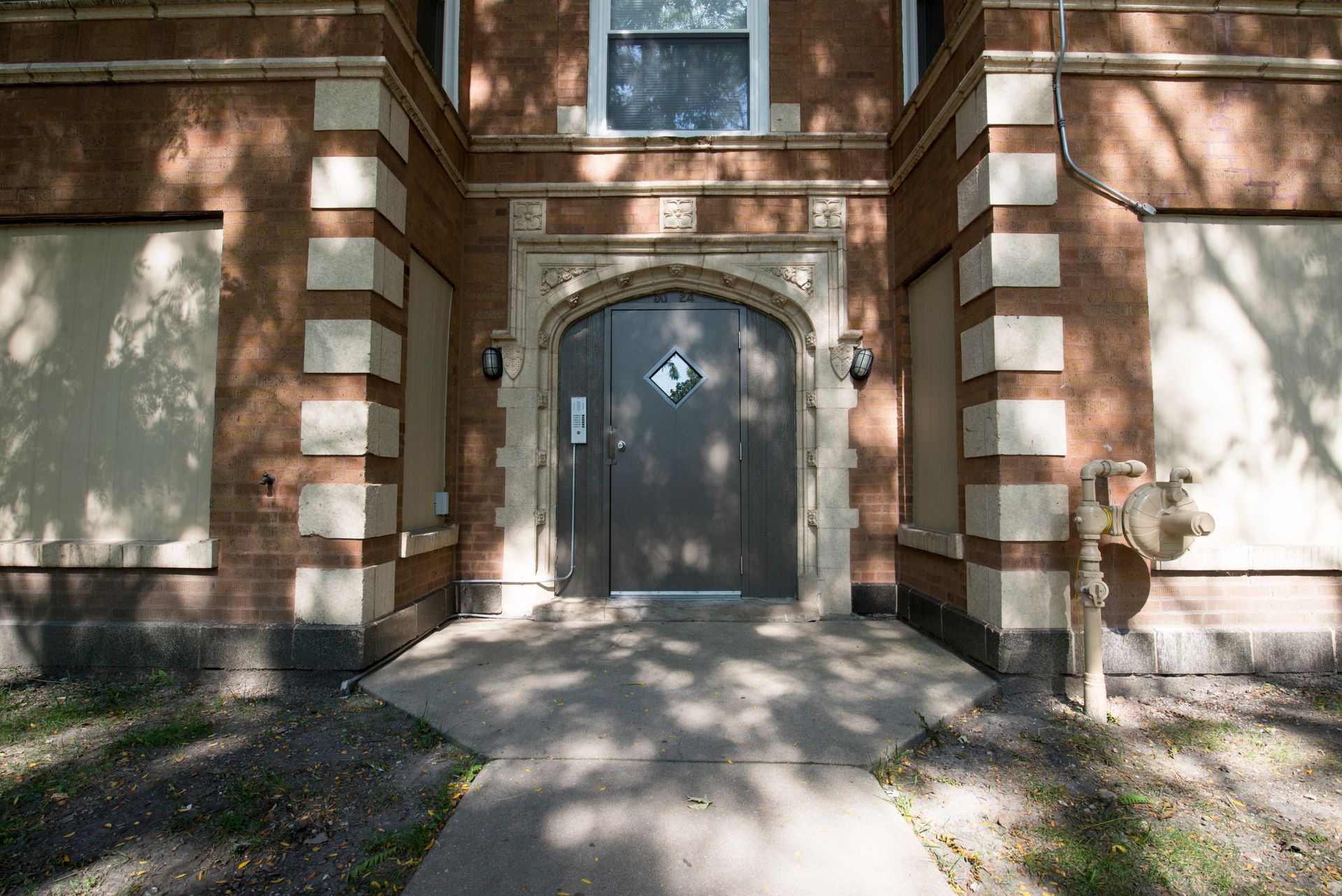 Brick building entrance with a gray door, flanked by boarded-up windows and an old fire hydrant.