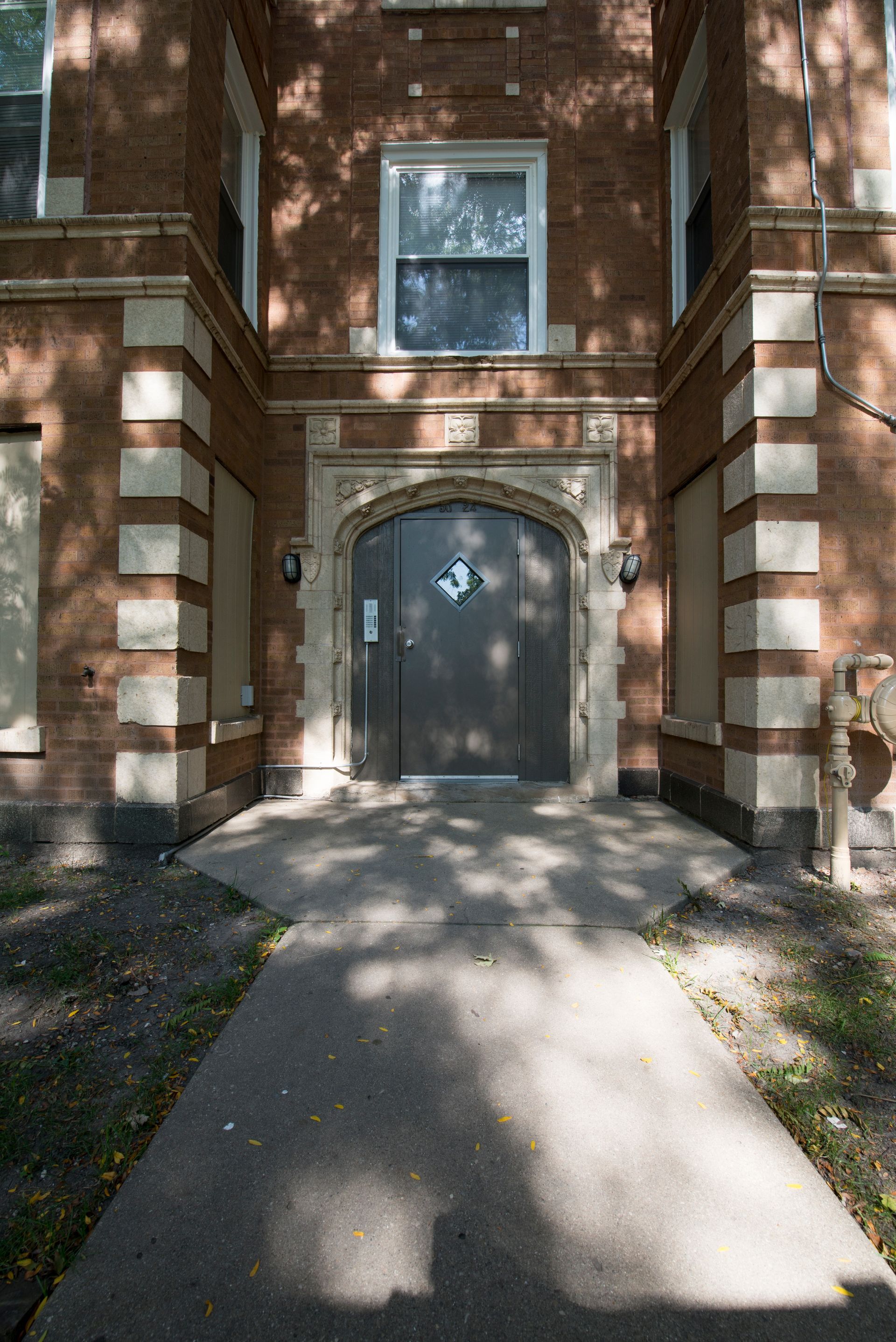 Brick building entrance with a concrete path leading to a dark door, flanked by ornate pillars.
