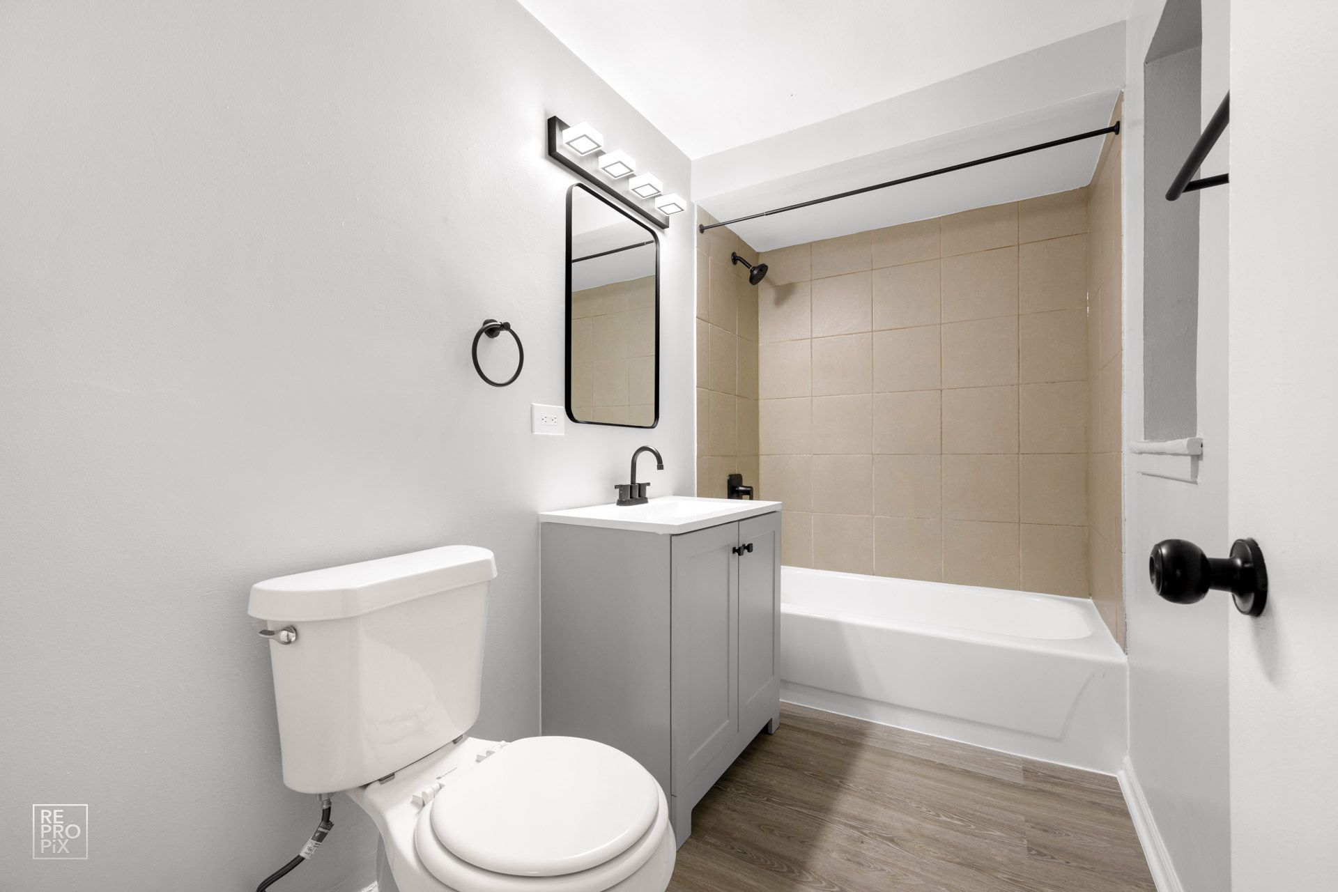 Bathroom with gray vanity, white toilet, and beige shower tiles. Black accents.