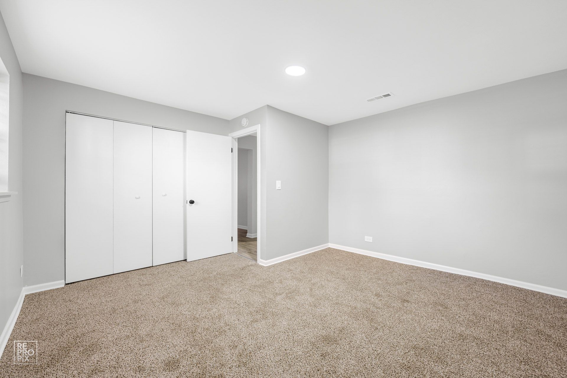 Empty bedroom with light gray walls, white closet doors, and tan carpet.