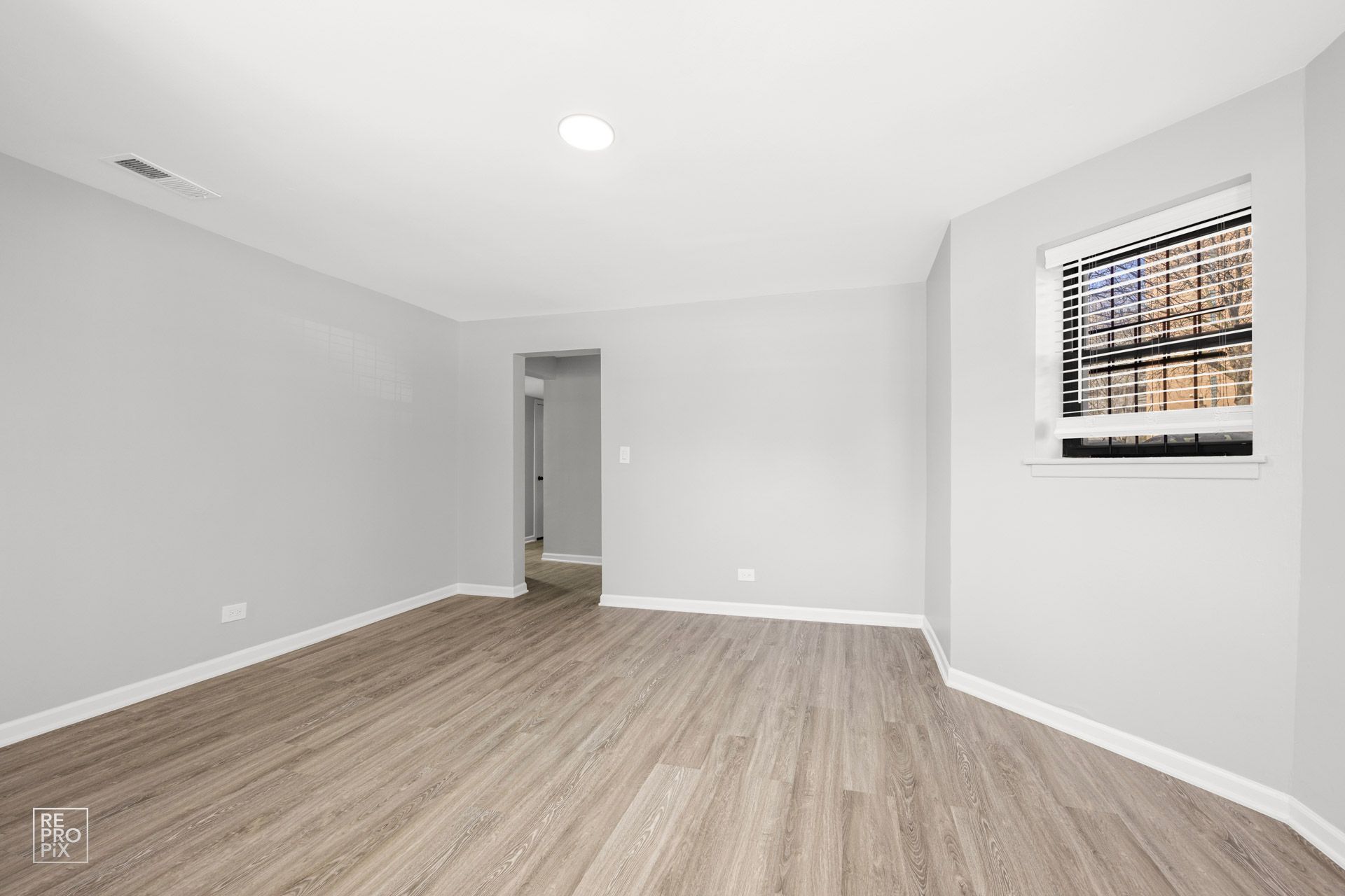 Empty room with light wood-look flooring, gray walls, doorway, and window with security bars.