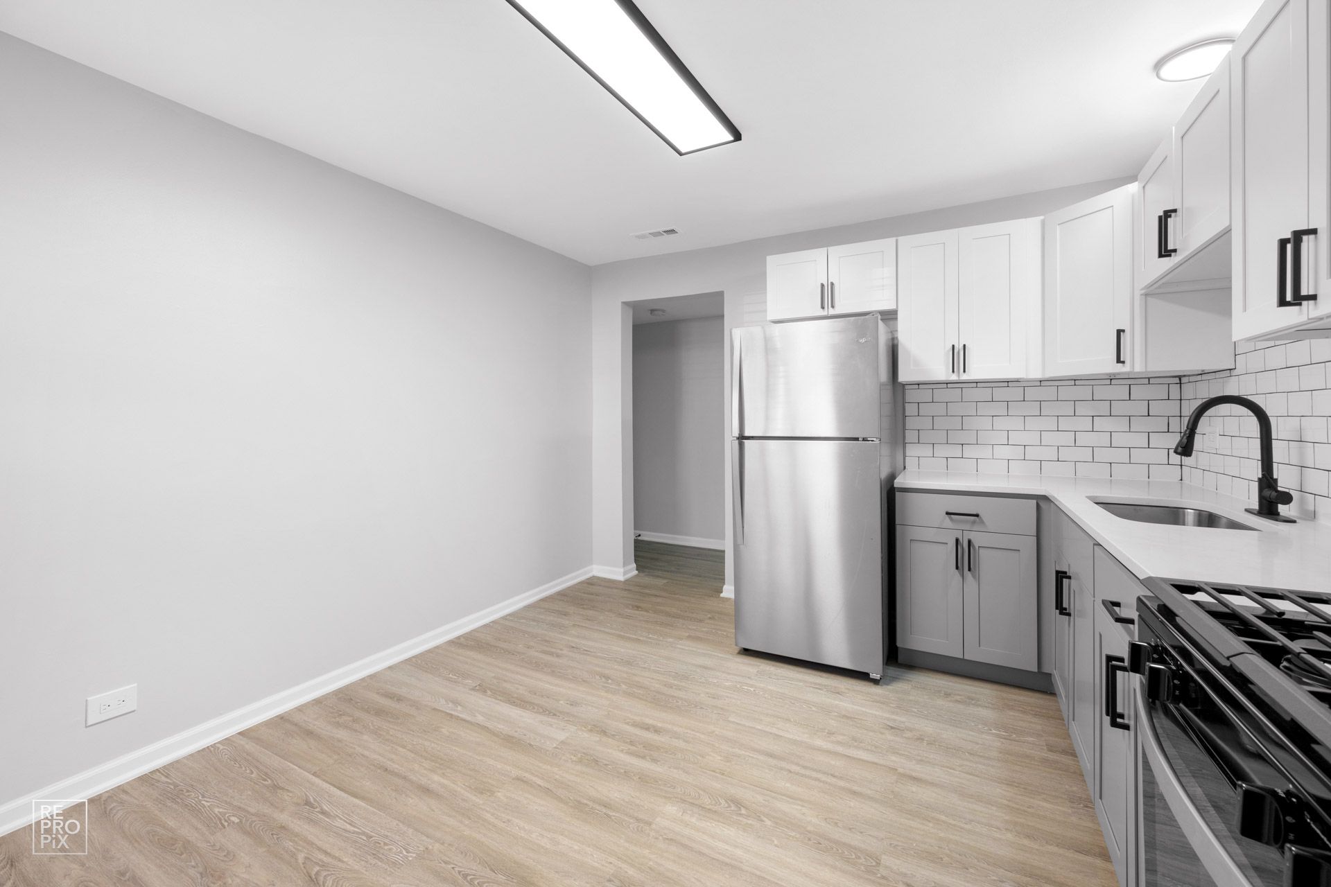 Kitchen with gray cabinets, stainless steel refrigerator, and light wood flooring.