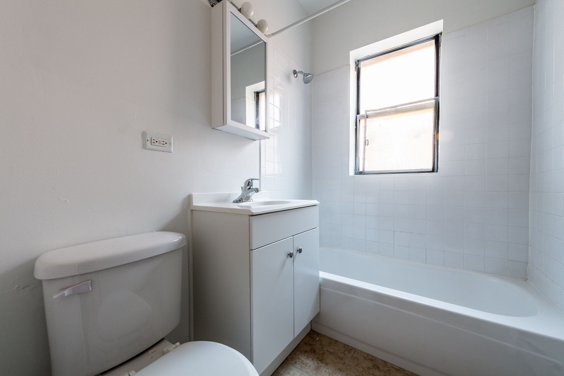 White bathroom with toilet, sink, medicine cabinet, and tub. Small window provides natural light.