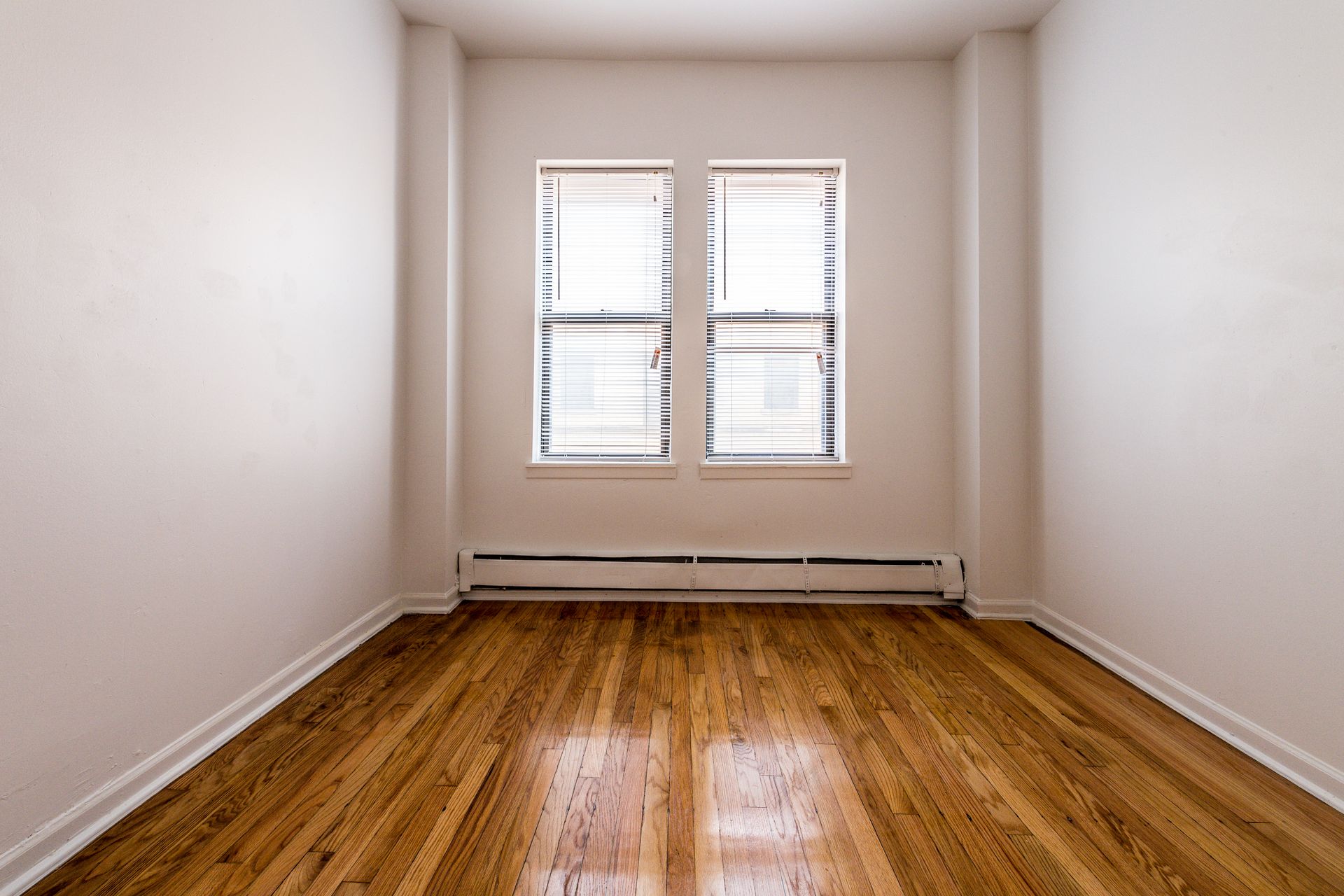 Empty room with wood floor, white walls, and a window with blinds.