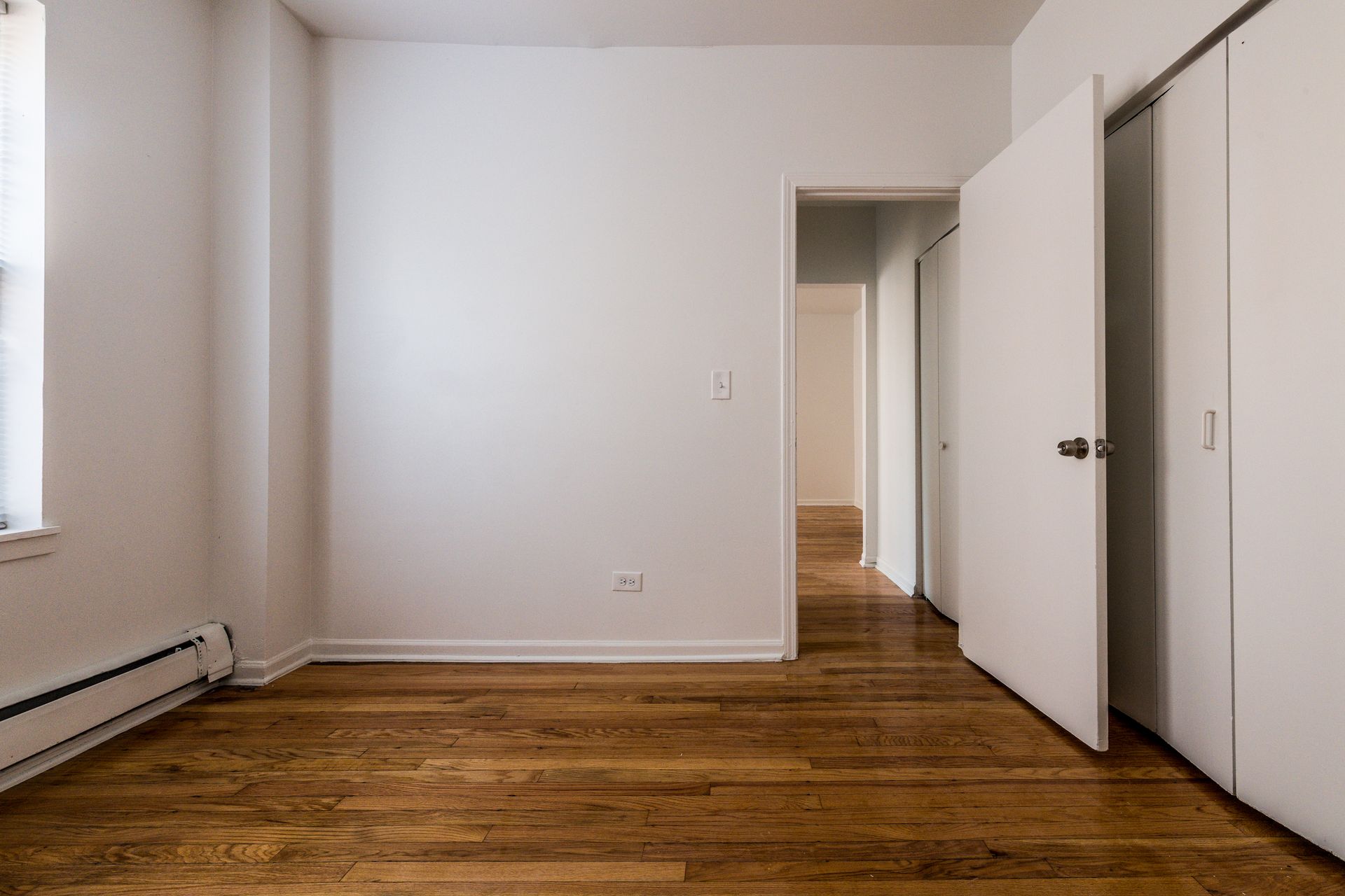 Empty room with hardwood floors, white walls, closet, doorway to another room.