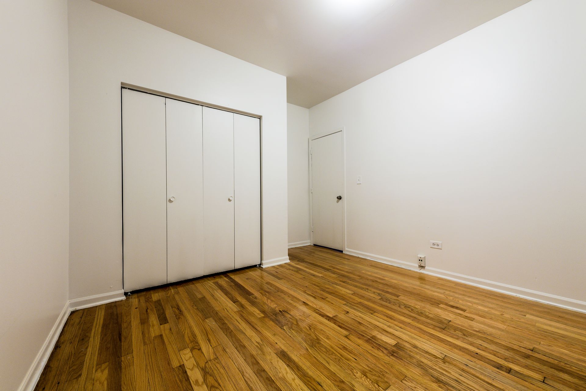 Empty room with hardwood floors, white walls, closet, and a closed door.