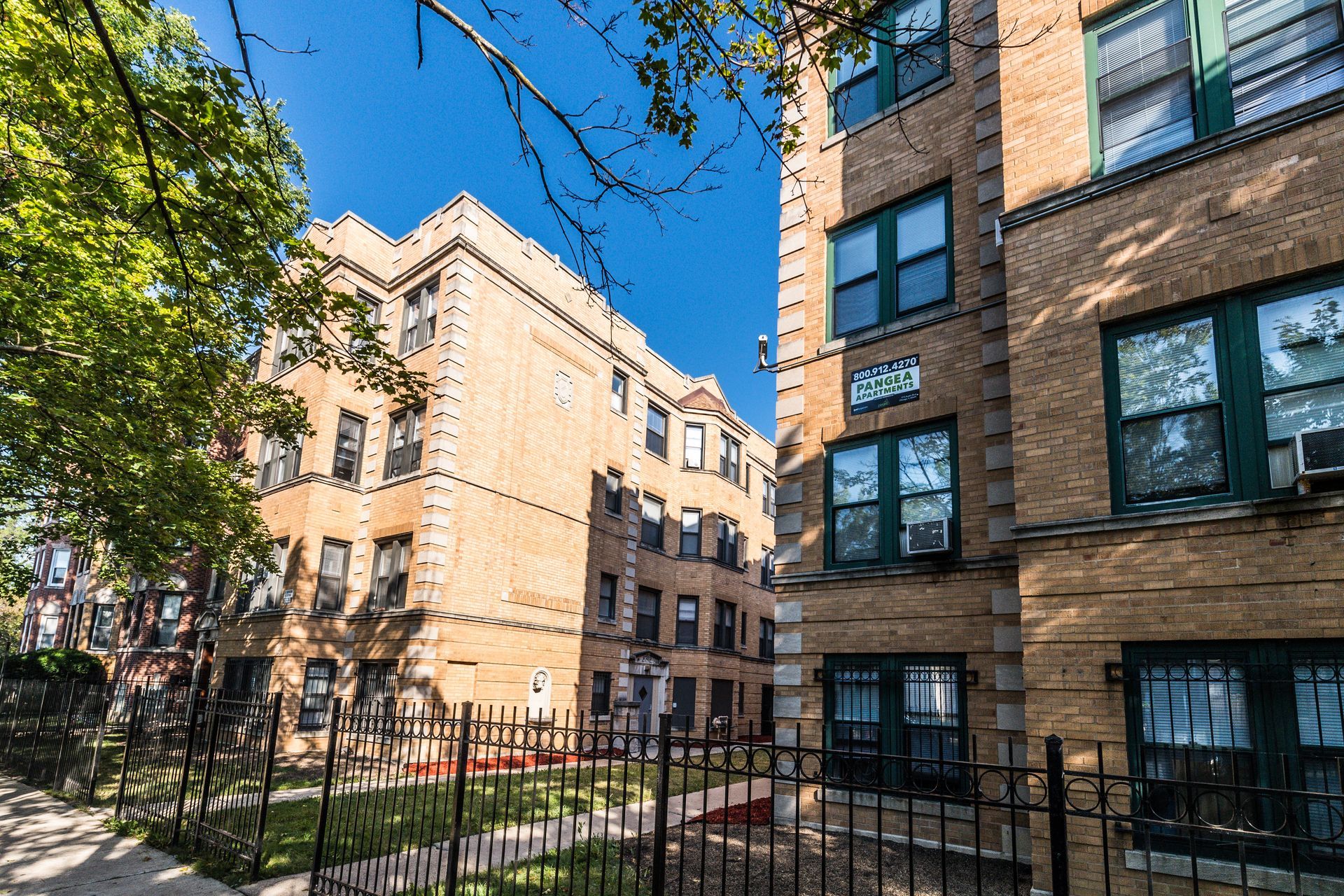 Buildings with brick facade, green windows, and wrought iron fence under a bright sky.