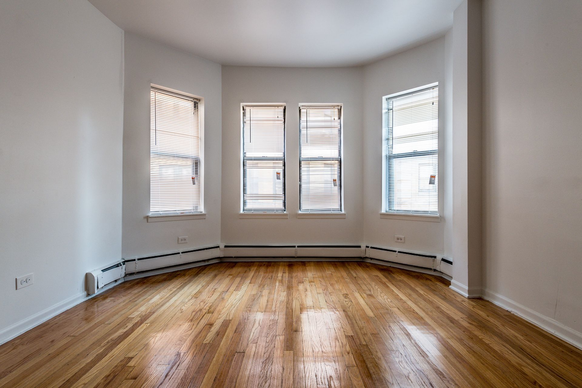 Empty room with bay window, hardwood floors, white walls, and radiator along the wall.