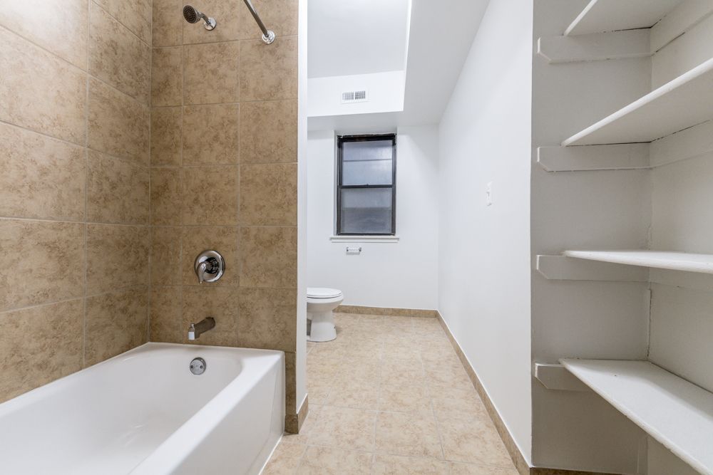 Bathroom with bathtub, showerhead, toilet, window, and built-in shelving.