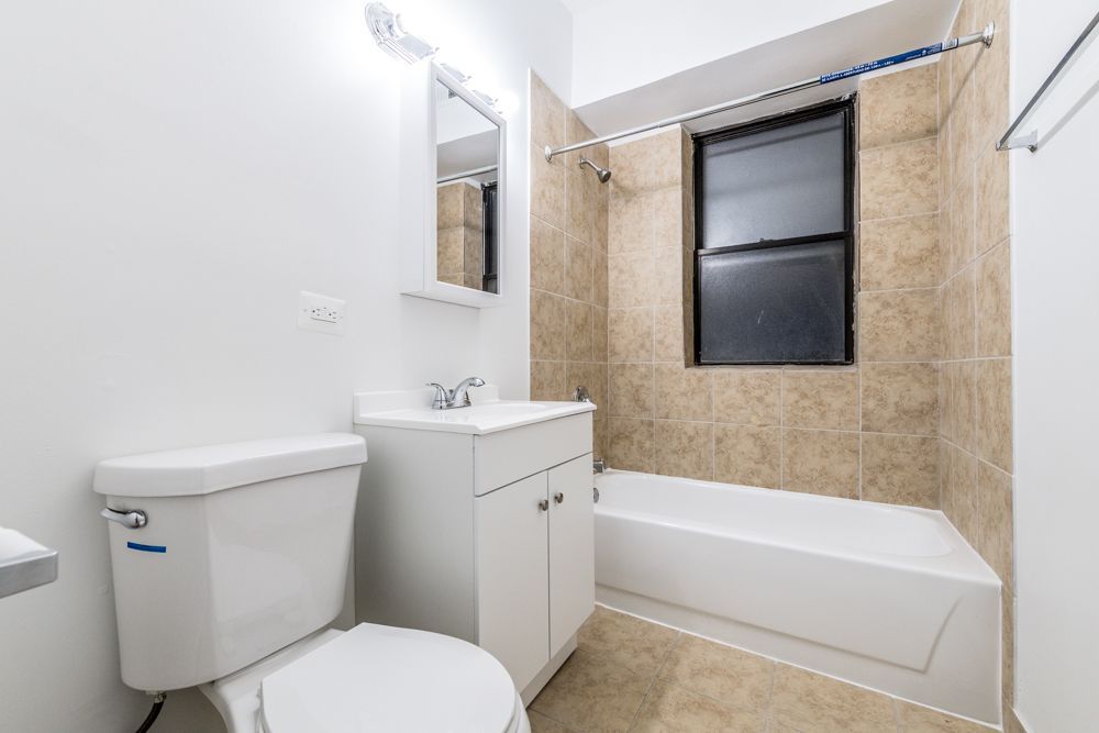 White bathroom with a toilet, sink, and bathtub. Beige tiled walls.
