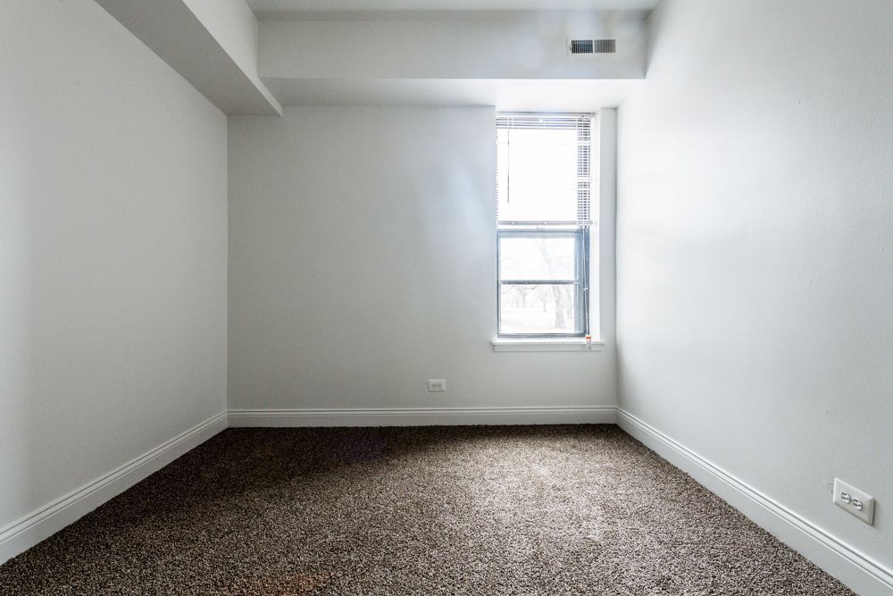 Empty room with brown carpet, white walls, and a window.