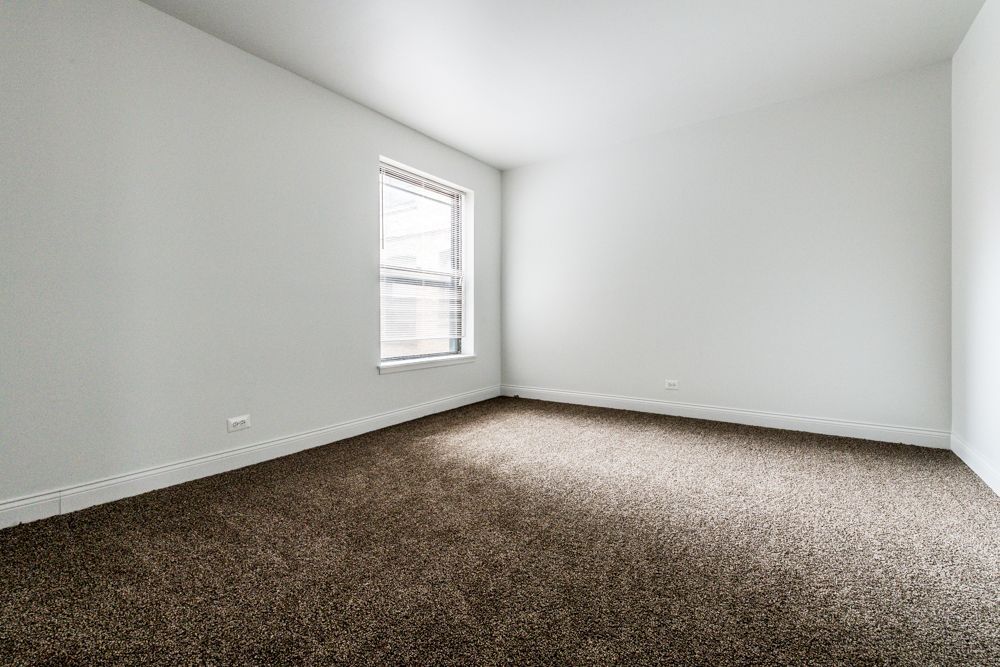 Empty room with brown carpet, white walls, and a window.