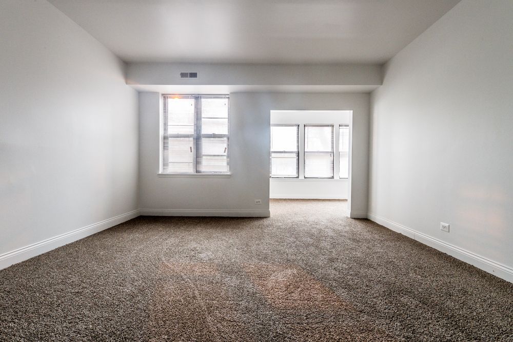 Empty room with brown carpet, white walls, and two windows.