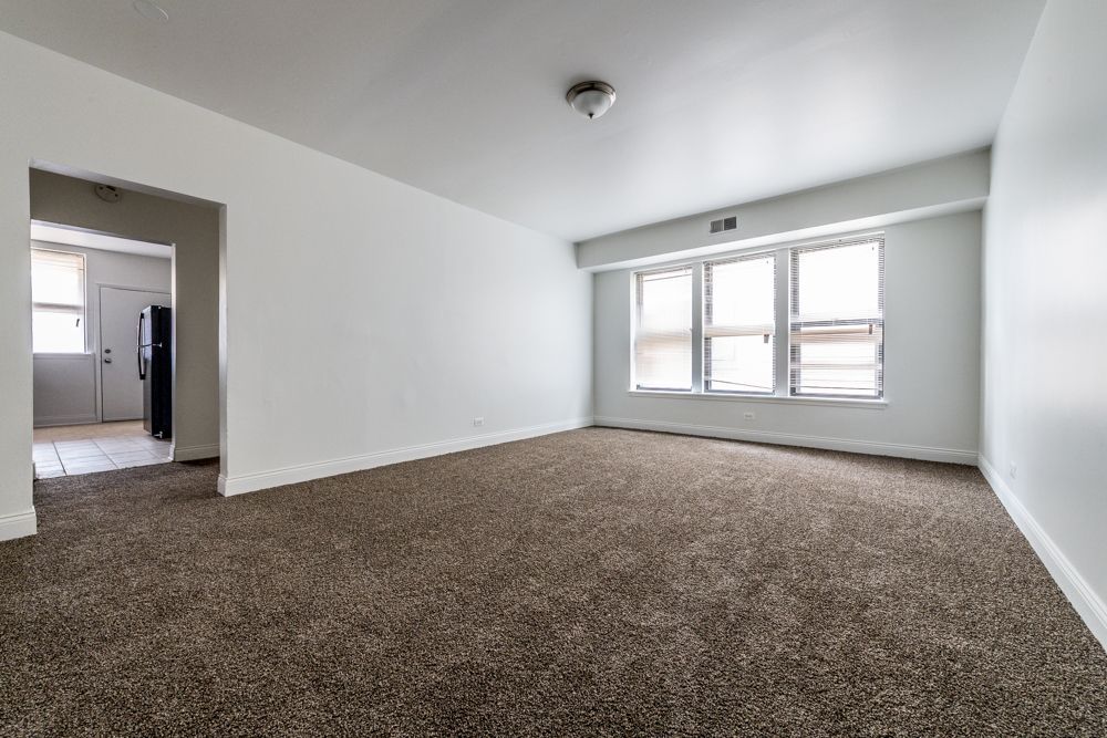 Empty living room with brown carpet, white walls, and a window.