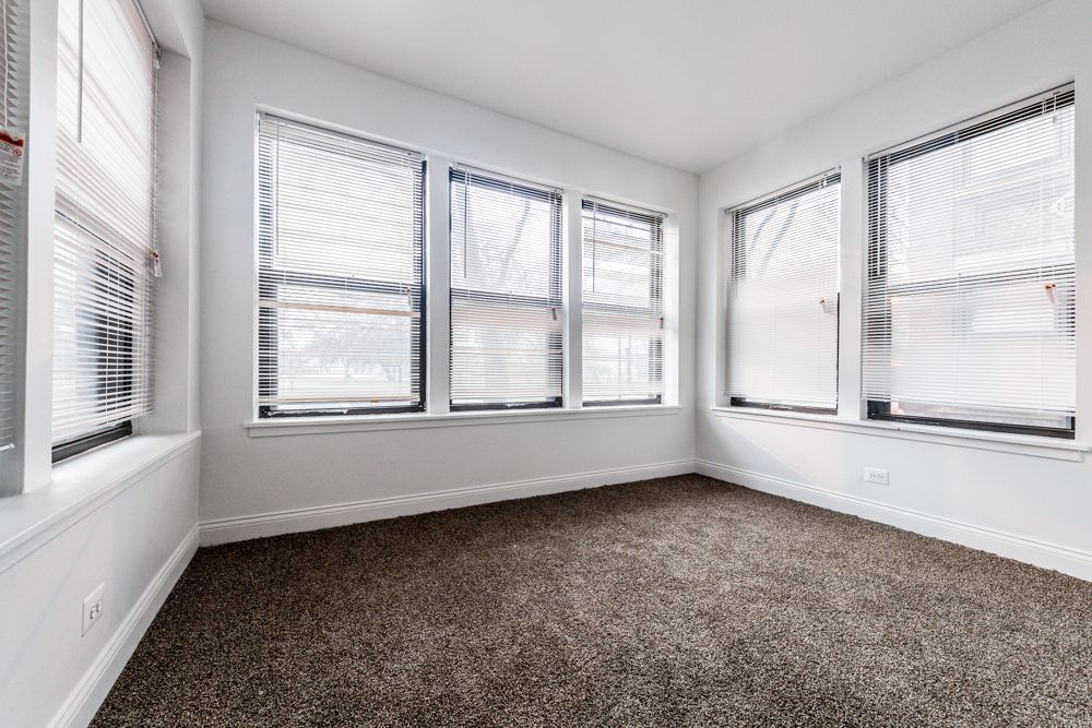 Empty room with carpet and multiple windows with blinds, gray walls.