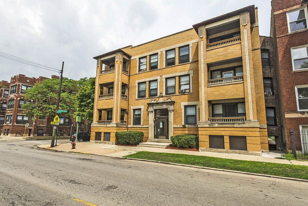 Three-story brick apartment building with balconies, street view.