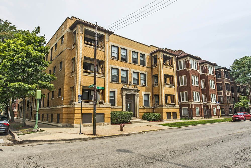 Apartment buildings on a city street, one yellow, one brown brick, overcast sky.