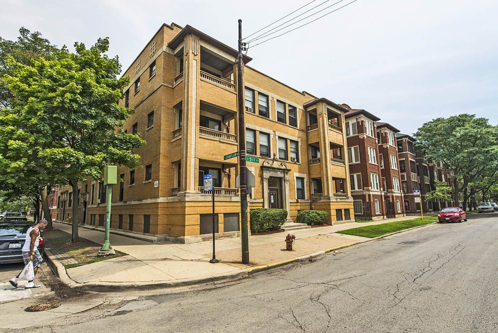 Apartment buildings on a street corner, one brick building is yellow, the other is red. A pedestrian walks by.