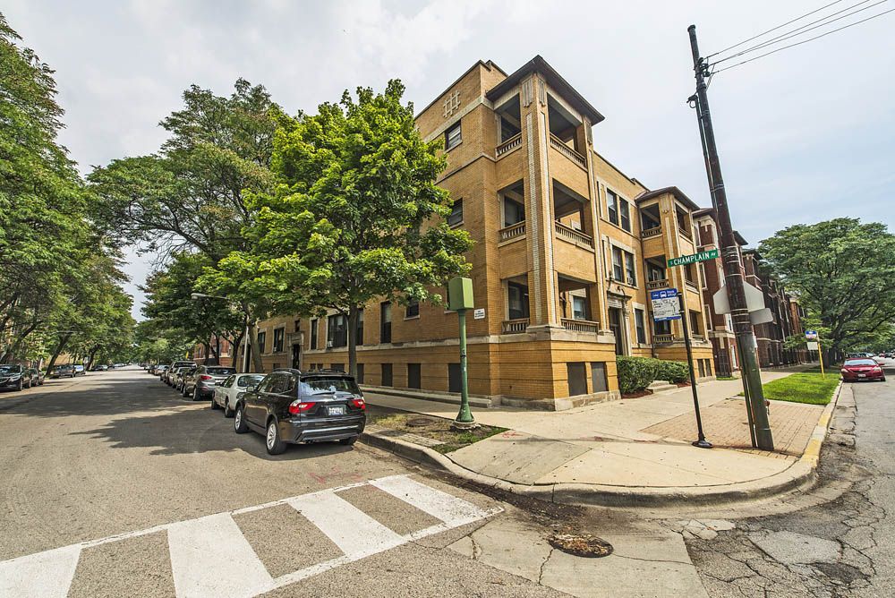 An apartment building on a corner lot; cars parked on the street; trees line the street.